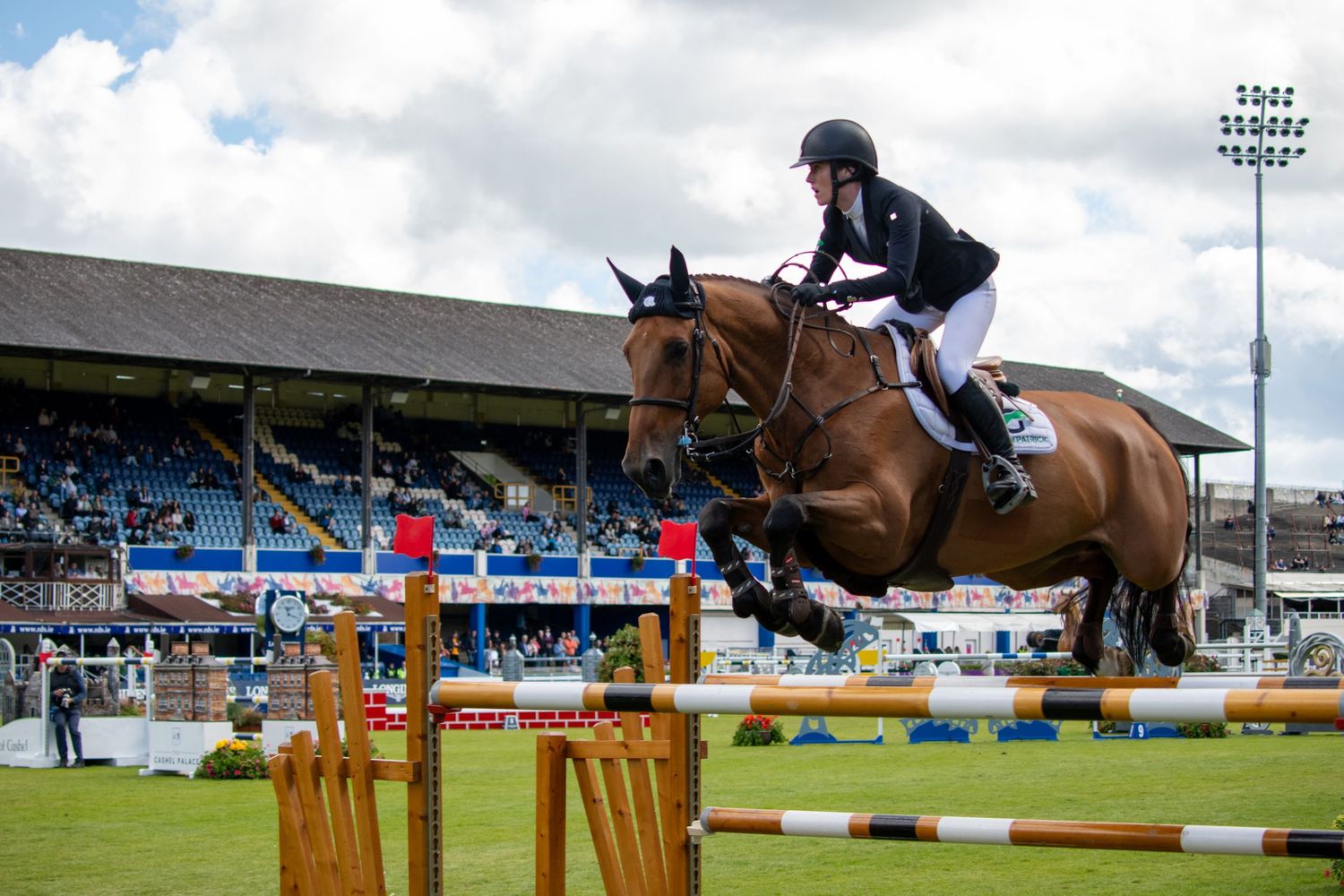 Competitive show jumping rider clearing a high yellow obstacle at an outdoor arena.