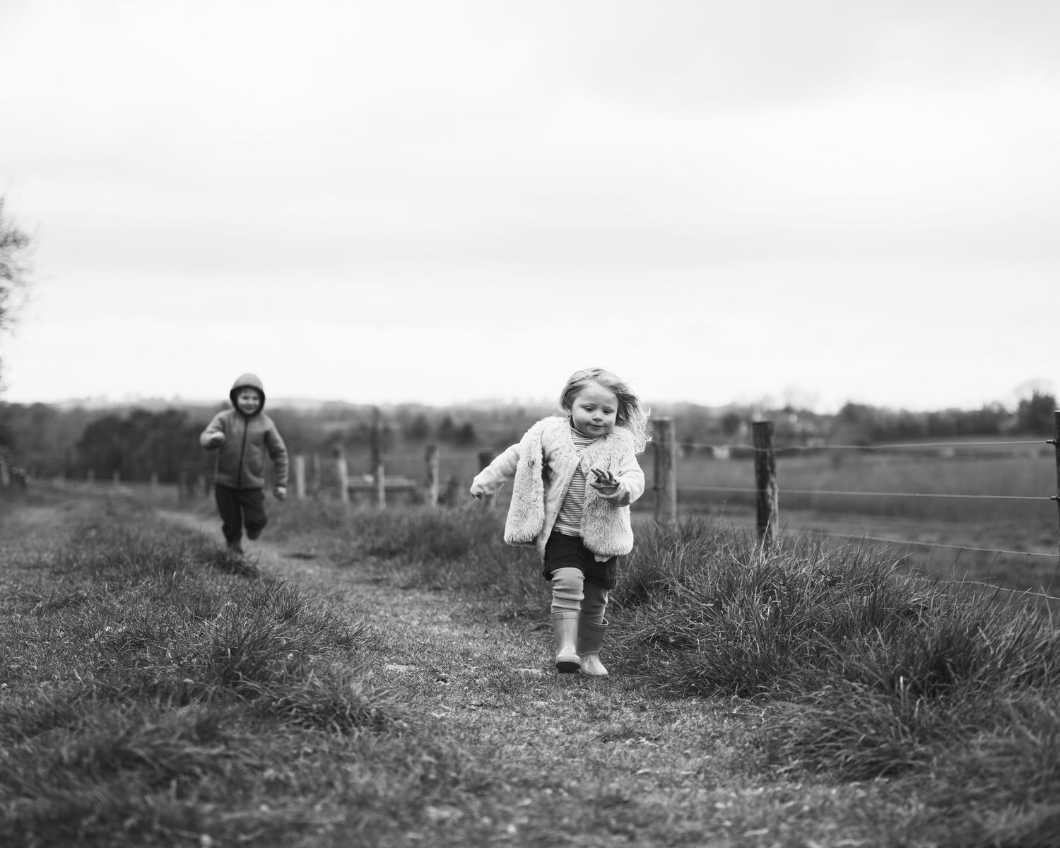 Black and white photograph of people running through a rural field.
