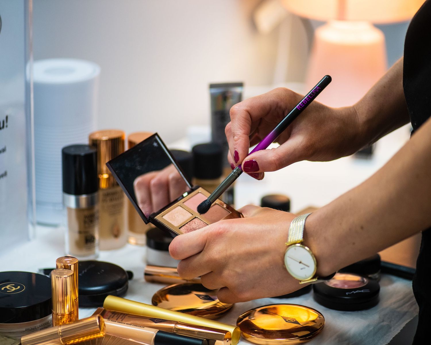 Close-up of hands applying makeup with brushes and cosmetic products on table.