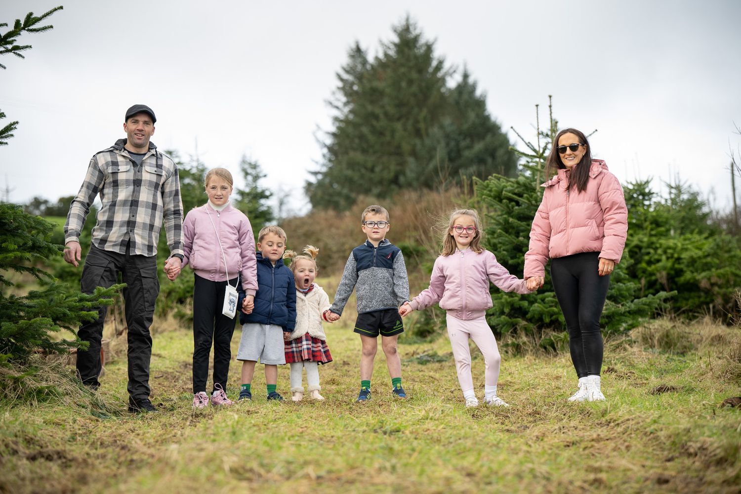 Family walking together on a hillside path surrounded by evergreen trees.