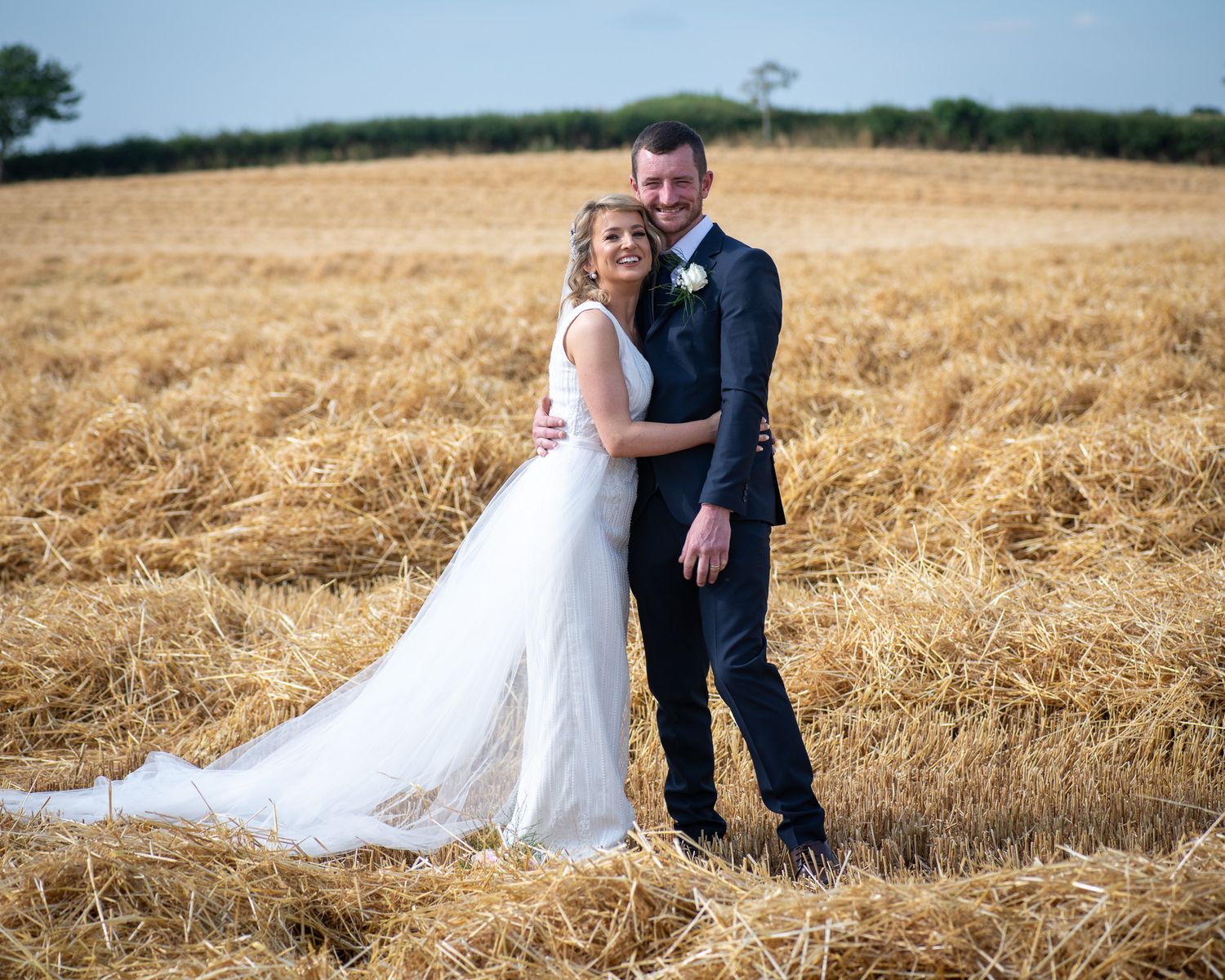 A wedding couple stands together in a golden wheat field on a bright summer day.