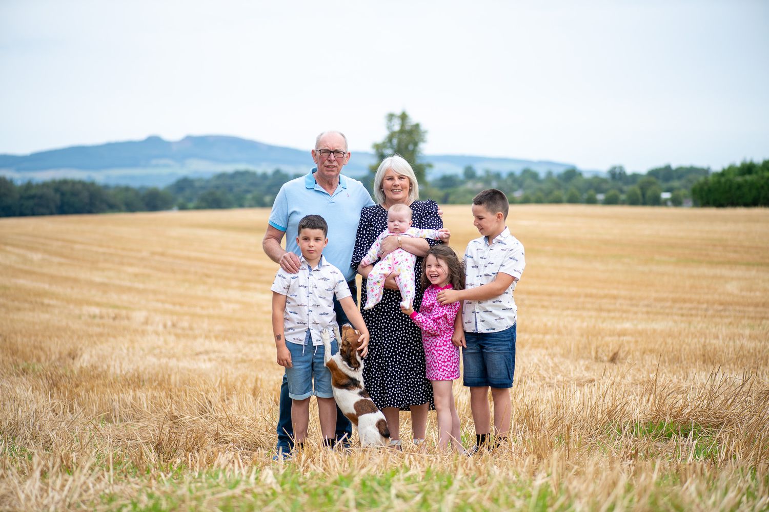 Group photo session in a golden wheat field during sunset with mountains in the distance.