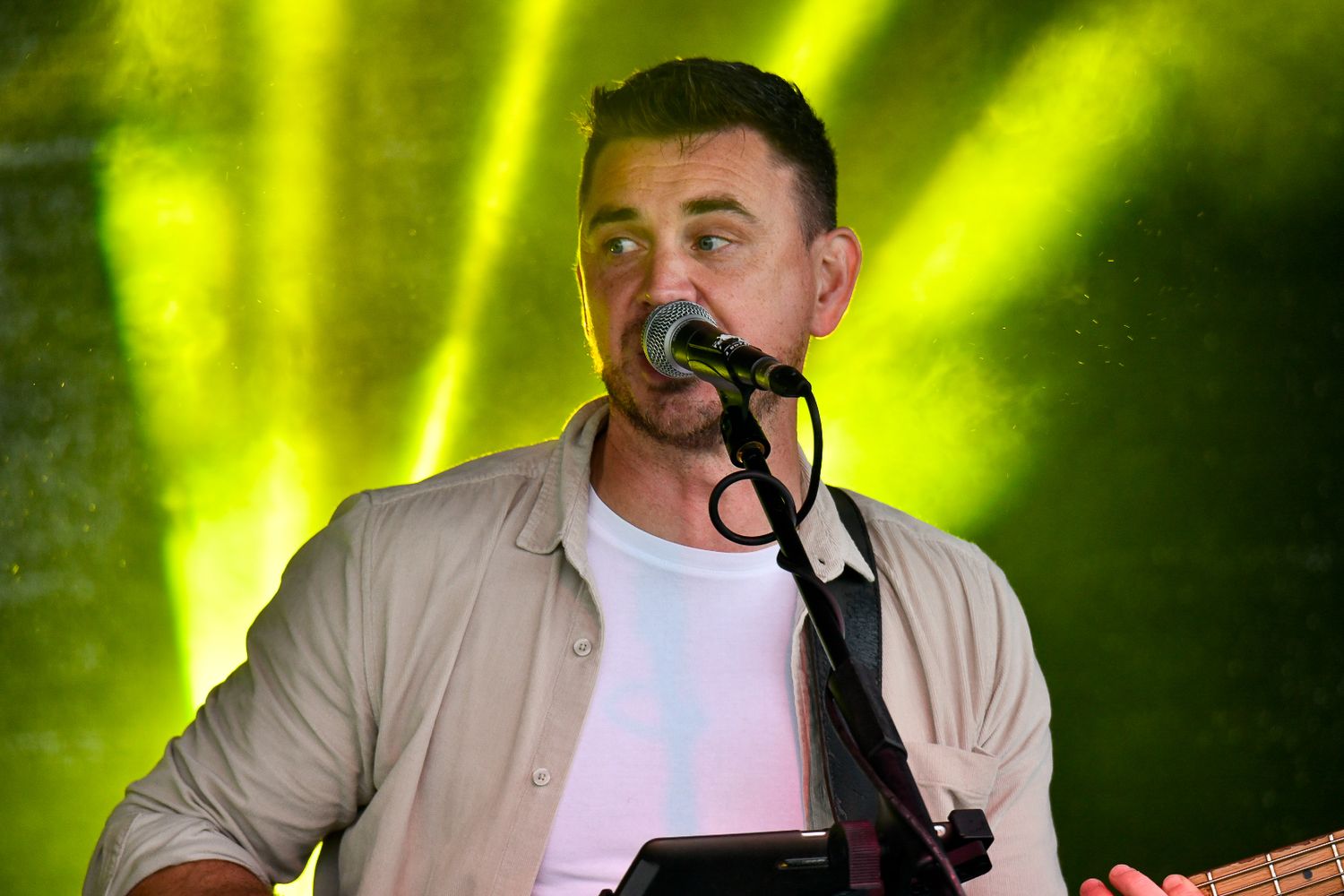 A performer sings into a microphone on stage with bright yellow lighting effects.