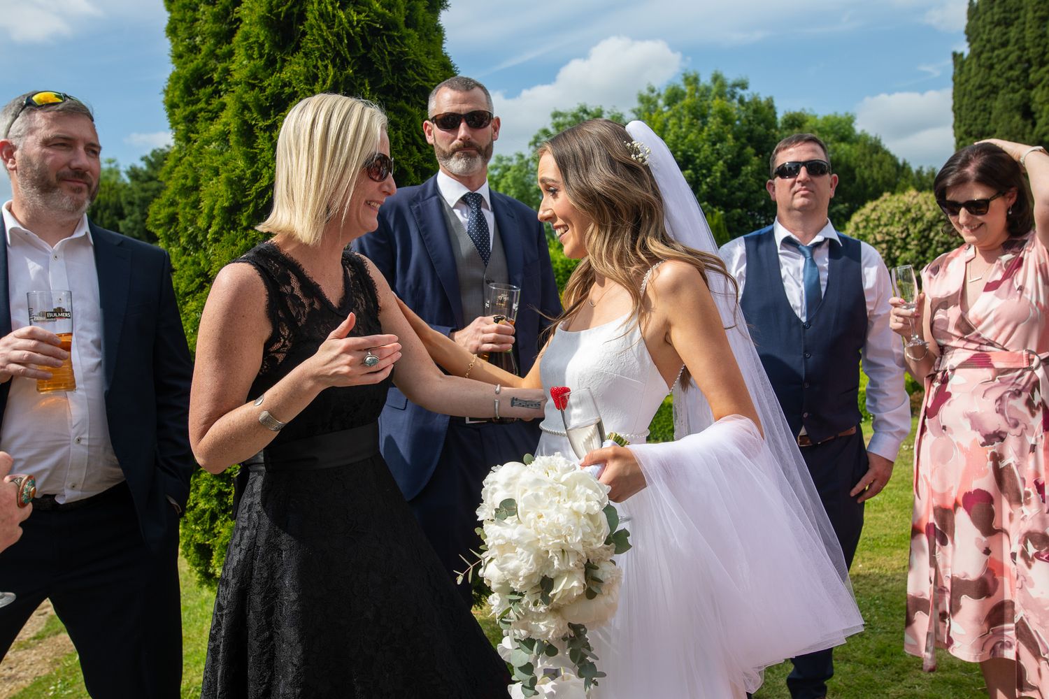 Wedding guests mingle on a sunny lawn during an outdoor reception celebration.