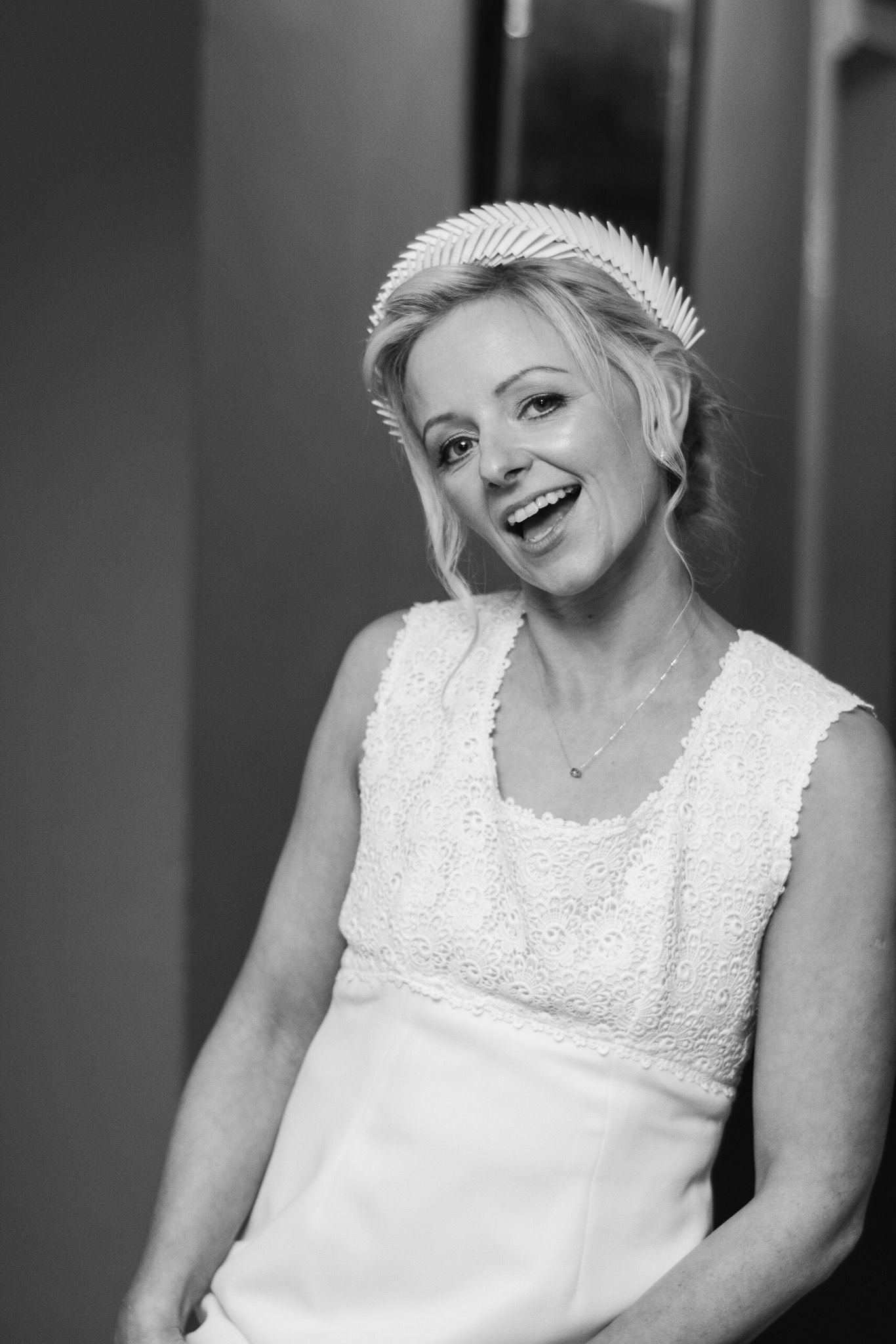 A bride wearing a white dress and headpiece smiles brightly in black and white.