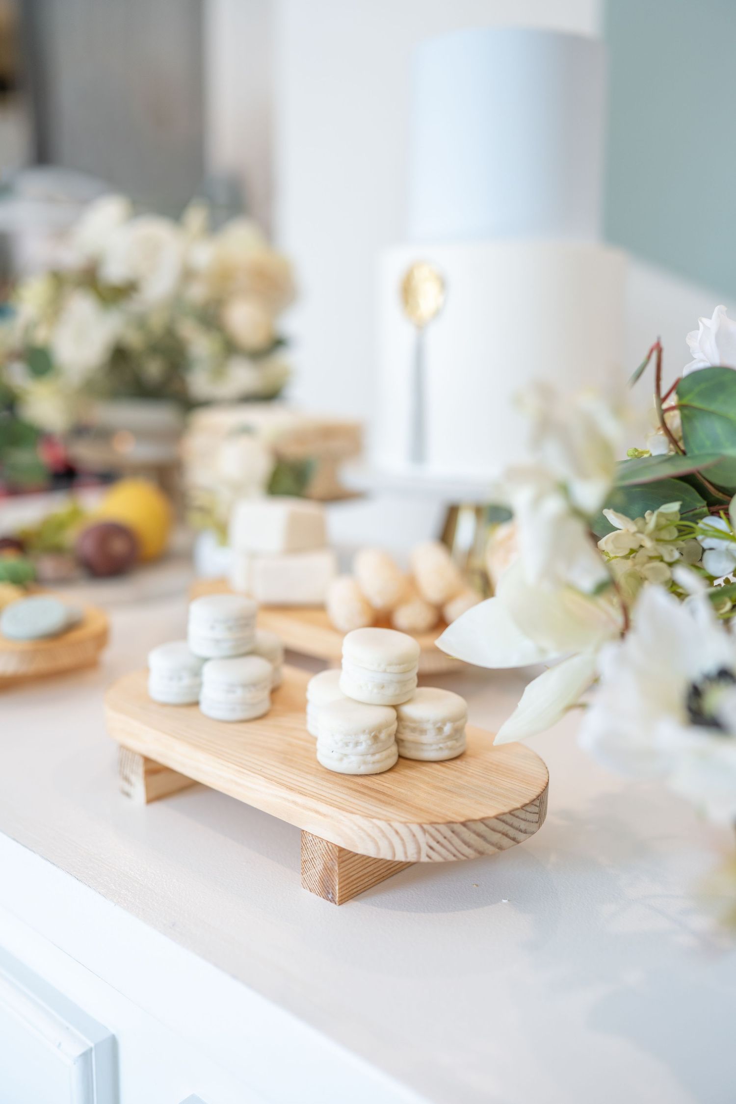Rustic wooden serving boards display macarons and treats on a white table with soft blue and floral accents.