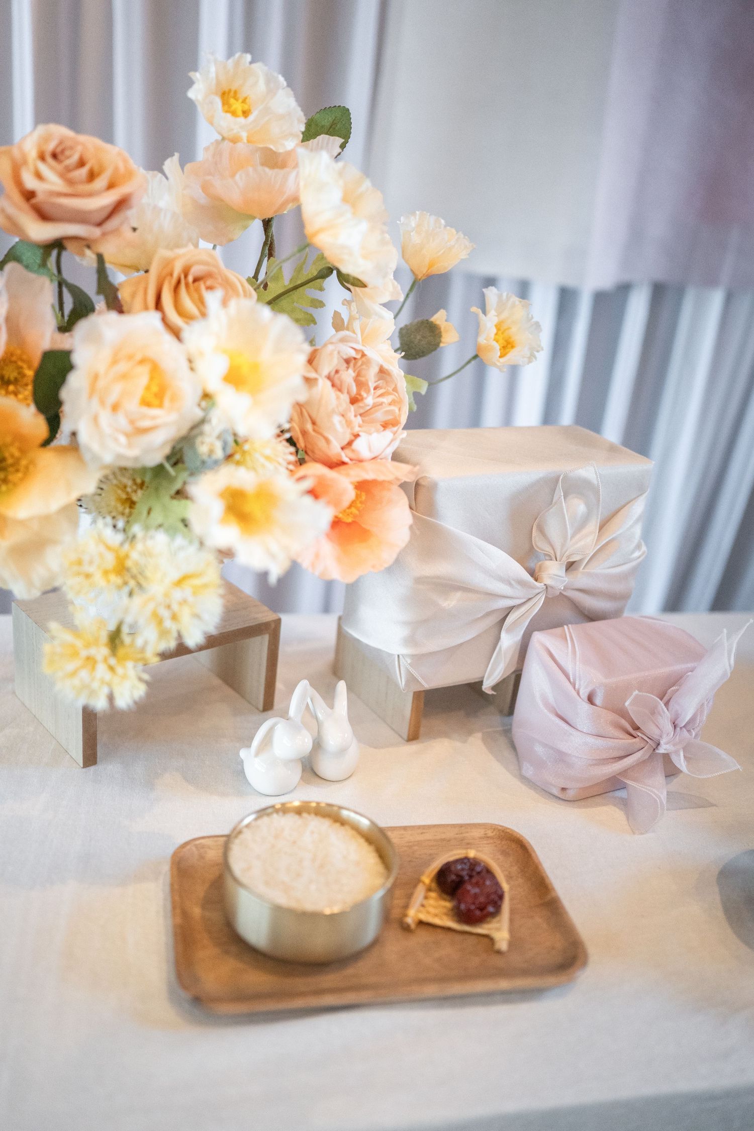Elegant dohl table setting with peach and cream floral arrangement, wrapped gifts, and dessert plate in soft natural light. Photographer