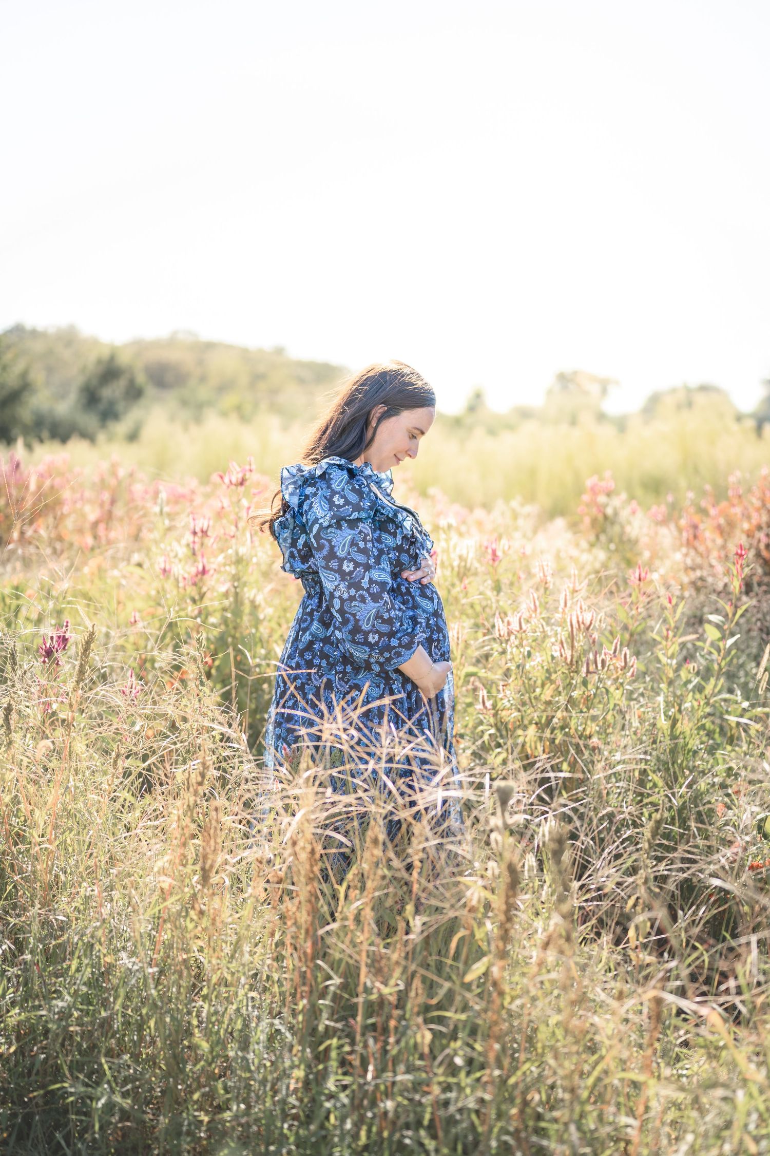 Woman in blue floral dress walks through a sunlit wildflower field on a summer evening.