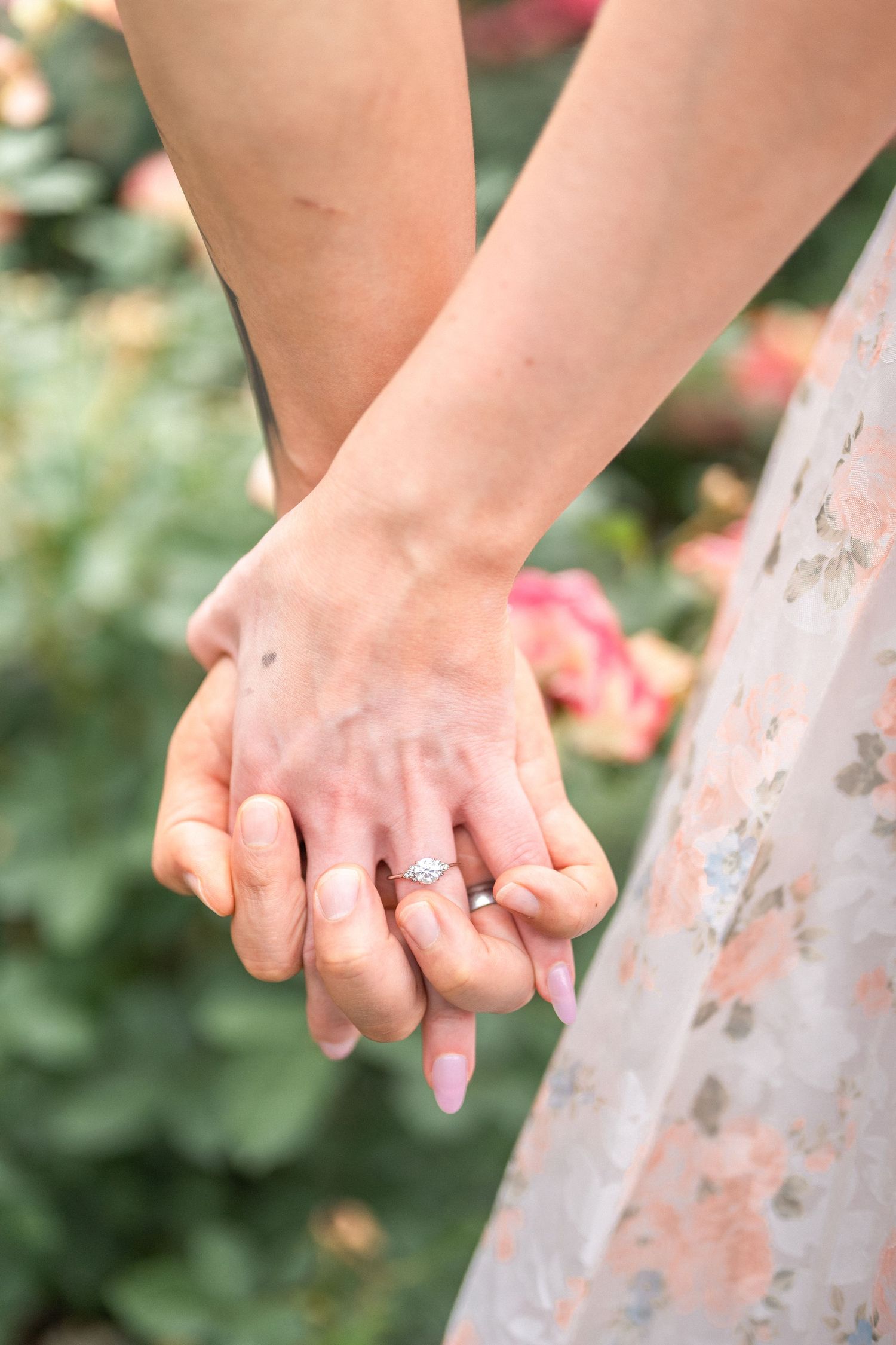 Engaged couple holds hands tenderly in garden setting with floral dress details visible. engagement Taylor Swift Travis Kelce