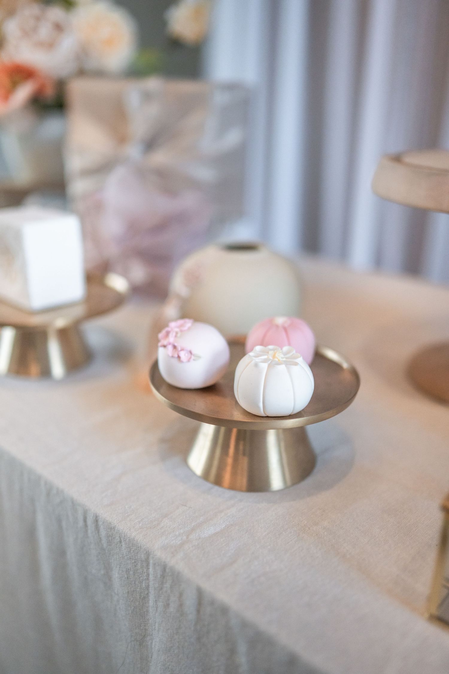 Small white macarons with delicate pink decorations displayed on elevated chrome cake stands against a light background. Dohl Nova Photo