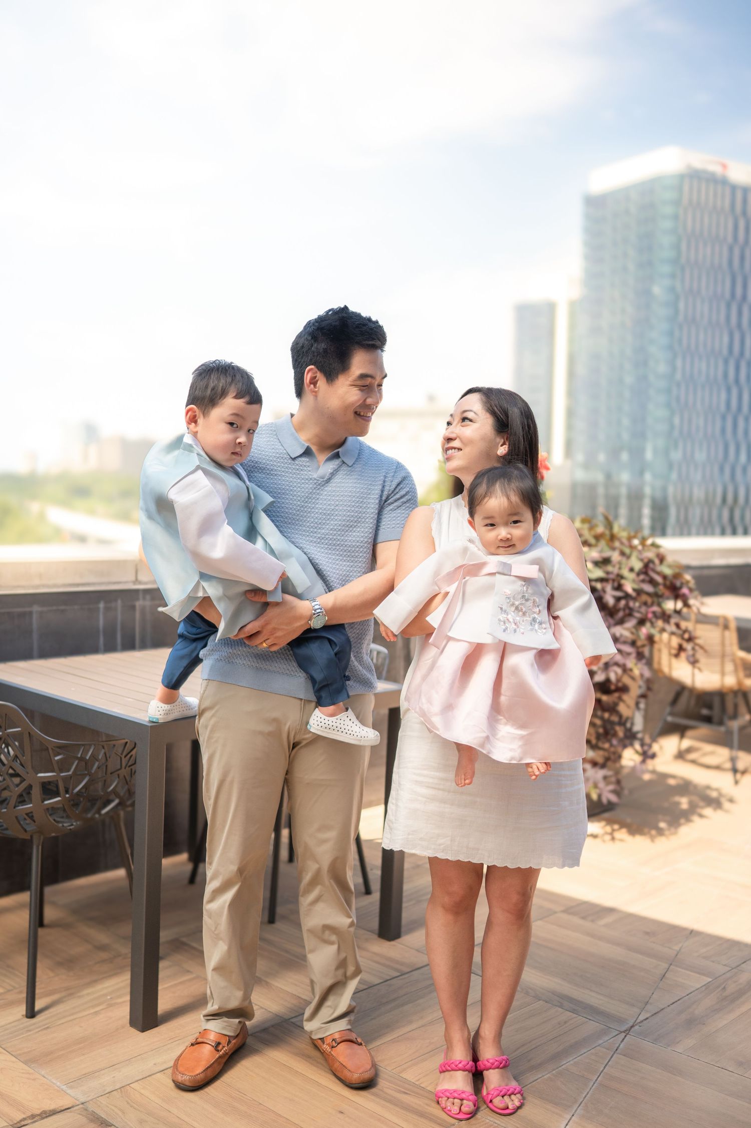 Family enjoying time together on an outdoor terrace with city buildings in the background on a sunny day. Leesburg photographer
