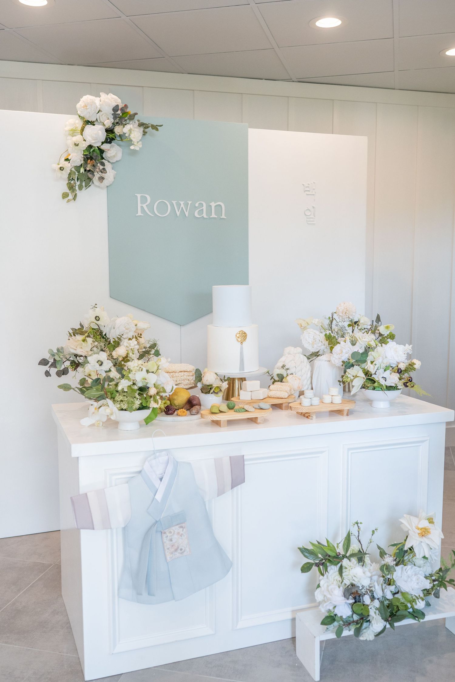 Elegant white wedding reception bar decorated with white flowers and greenery against a light blue accent wall.