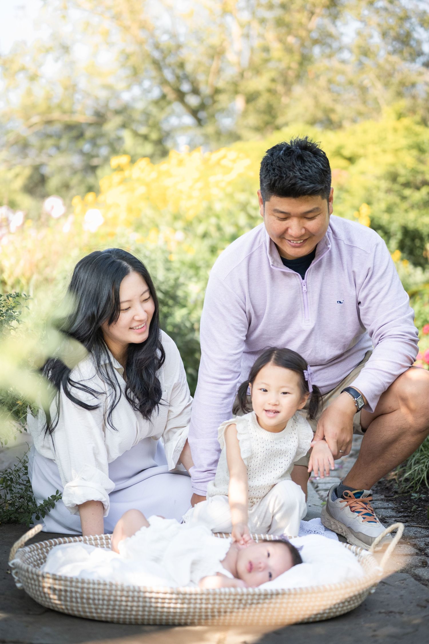 Family sitting outdoors together on a warm day with a baby nestled in a cozy gingham-patterned lounger. reston newborn photographer