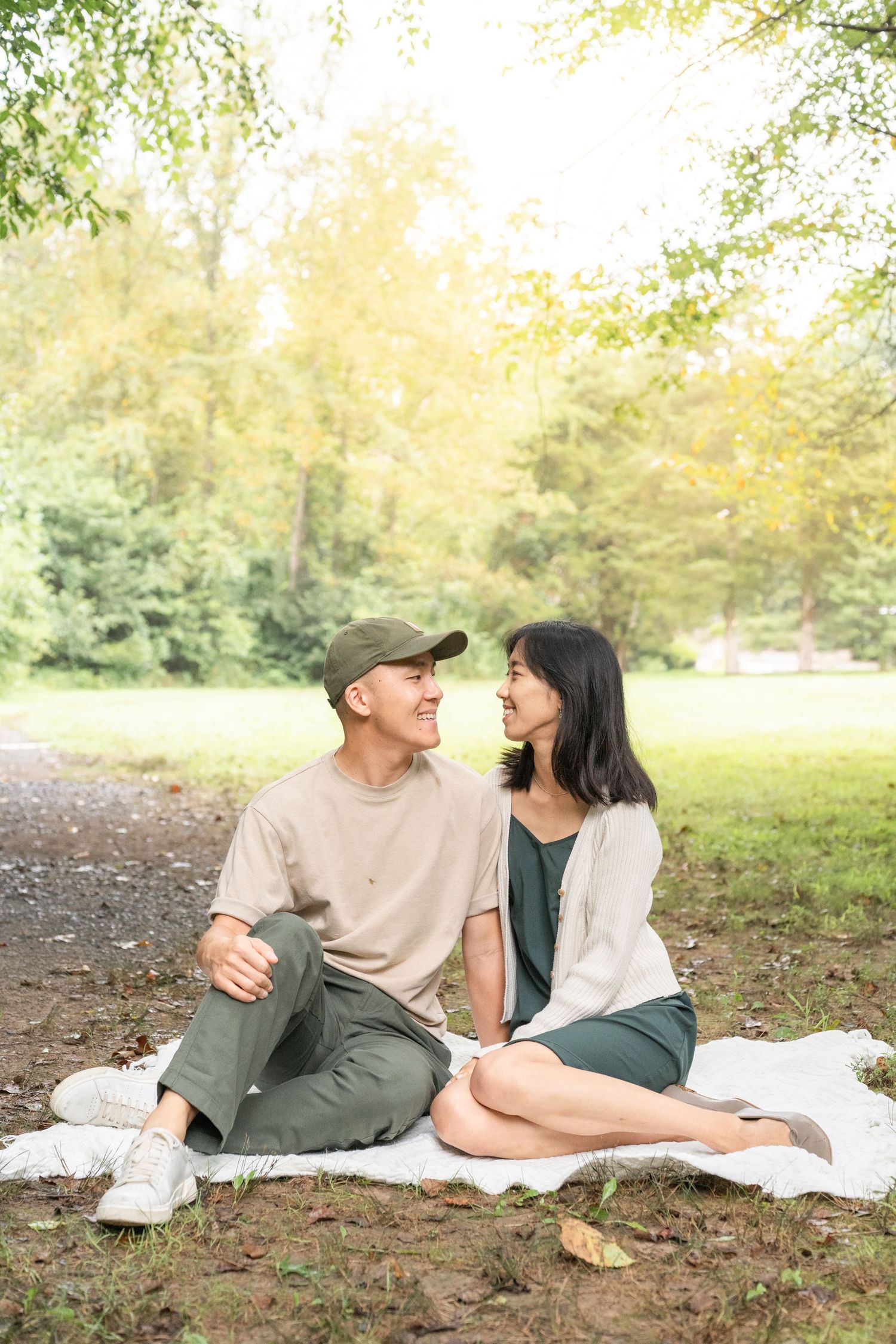 A couple relaxes on a picnic blanket in a sunlit park setting sharing intimate laughs and conversation.
