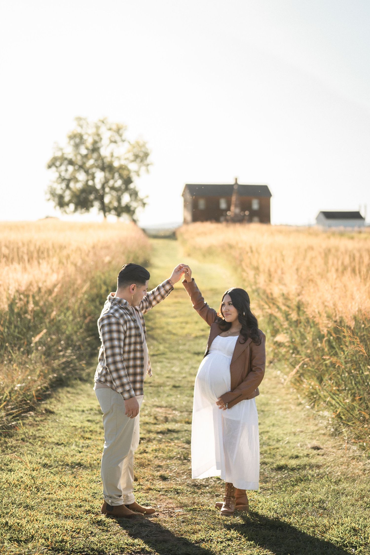 A couple embraces in a golden meadow at sunset while dancing together in a romantic outdoor setting.