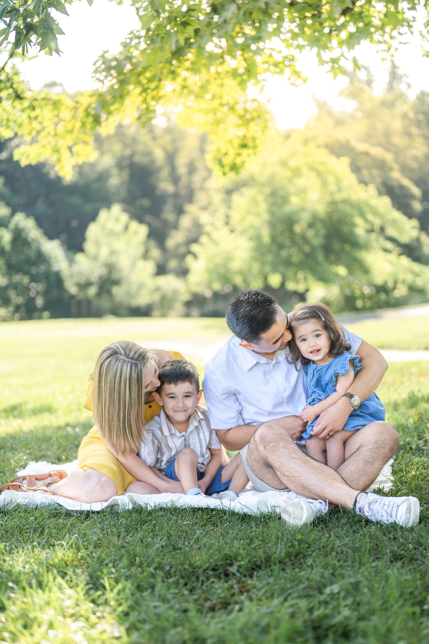 A family lounging together on green grass during a sunny day in a park setting. Northern virginia photographer