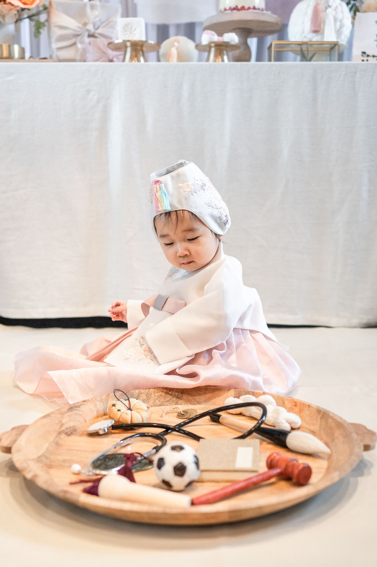 A baby in hanbok sits on a large wooden circular surface with toys and blankets around them for a doljabi. Reston photographer