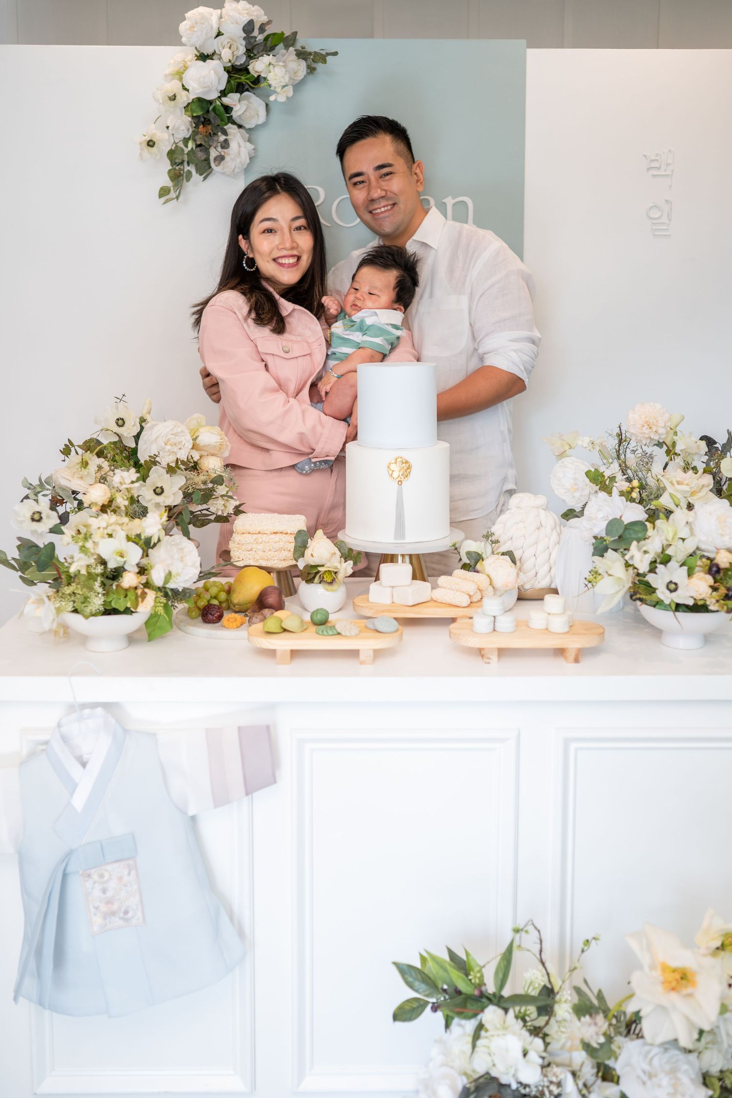 A family celebration featuring white floral decorations, a pristine cake display, and soft pink and pastel color scheme.