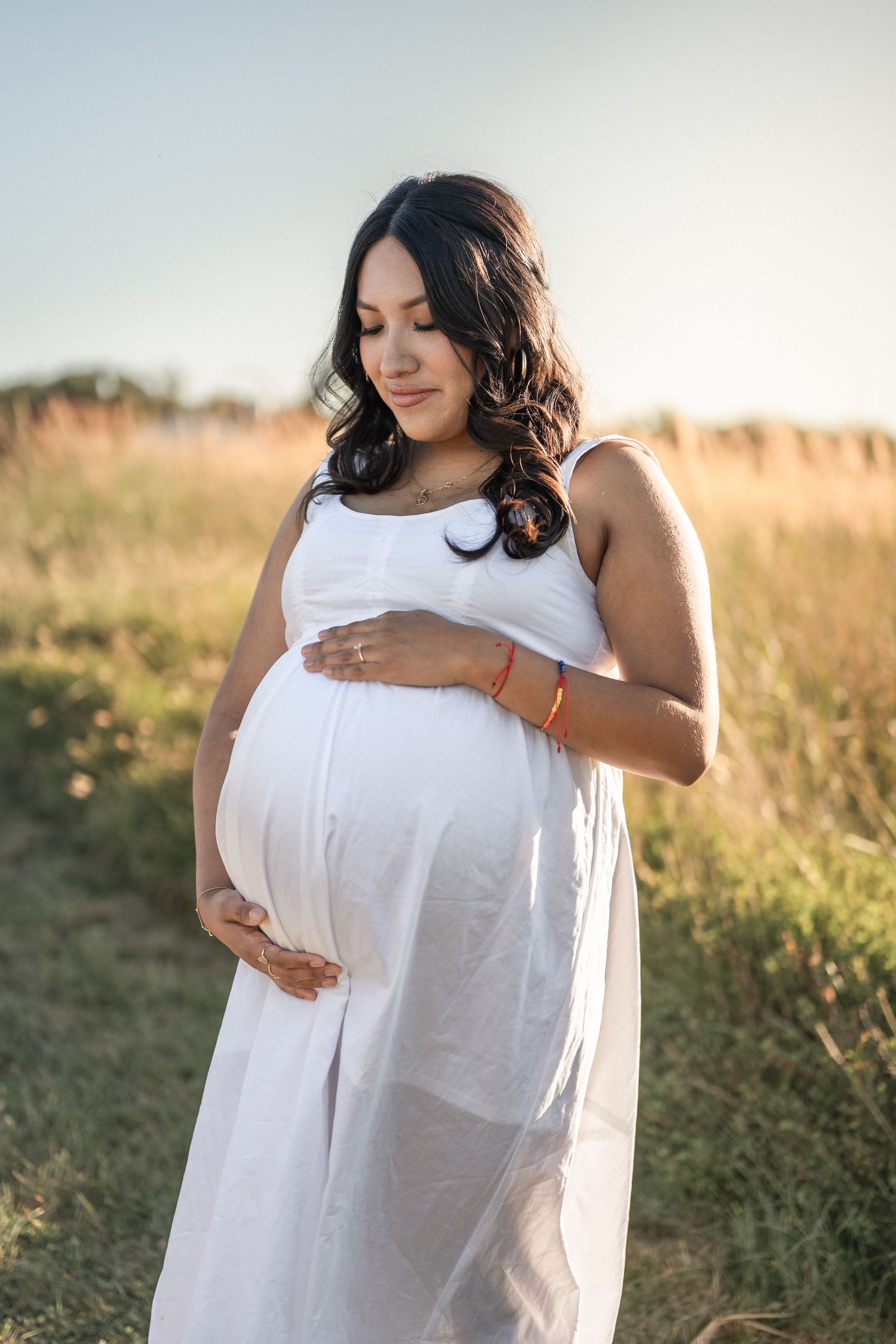 A series of ethereal maternity photos show someone wearing a flowing white dress in a golden sunlit field.