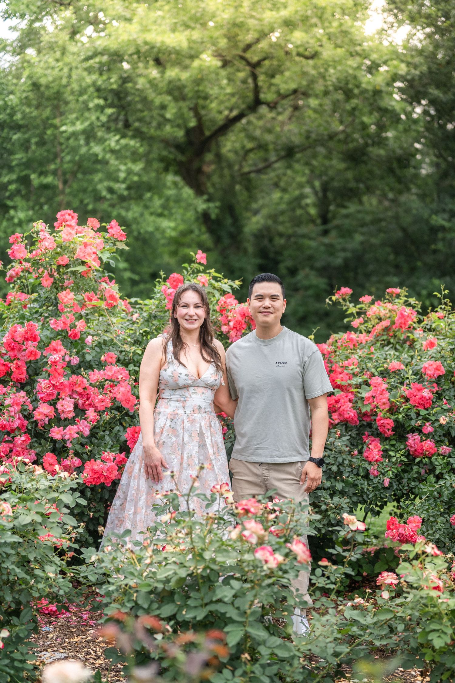 A couple poses for a portrait surrounded by vibrant pink roses in a garden setting. Northern Virginia Family Photographer Taylor Swift