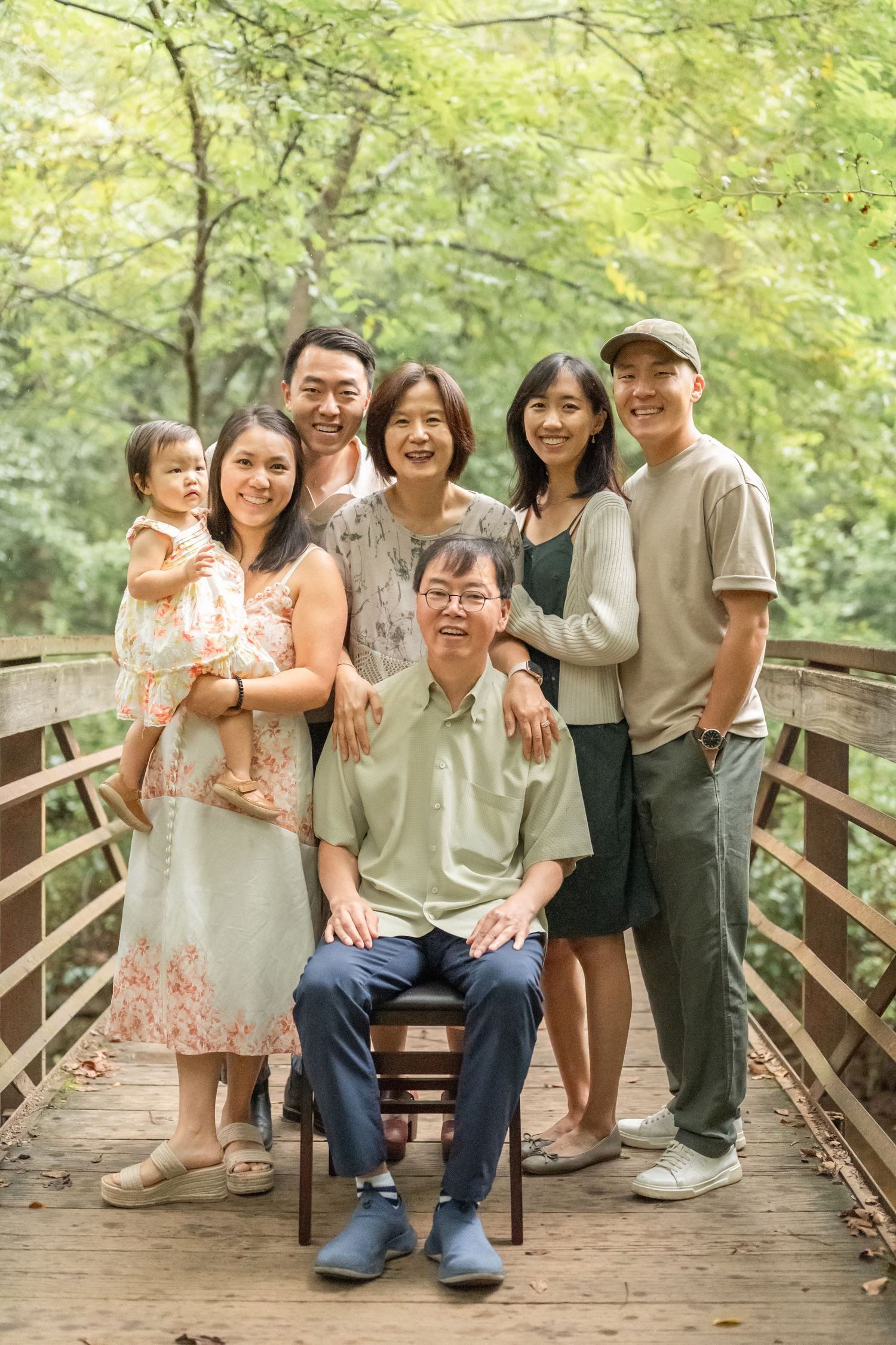 Extended family gathering on a wooden bridge in a park setting wearing coordinated neutral colored outfits.