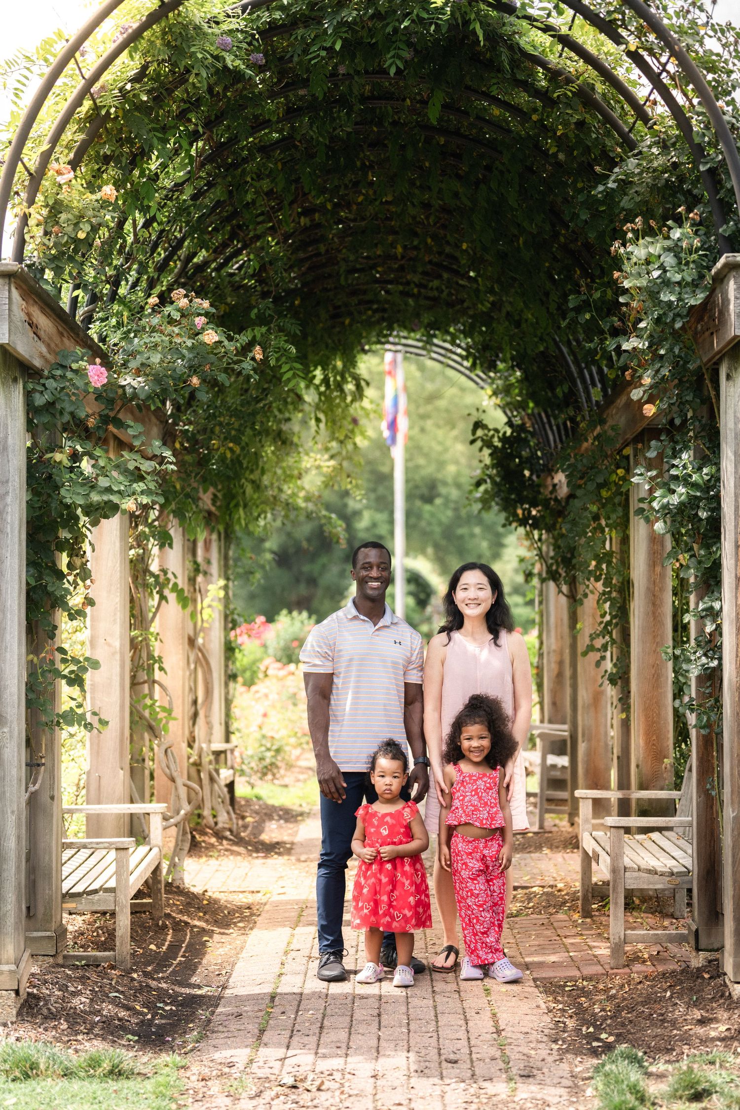 A family walks together under a beautiful garden archway covered in greenery. Northern Virginia Family Photographer