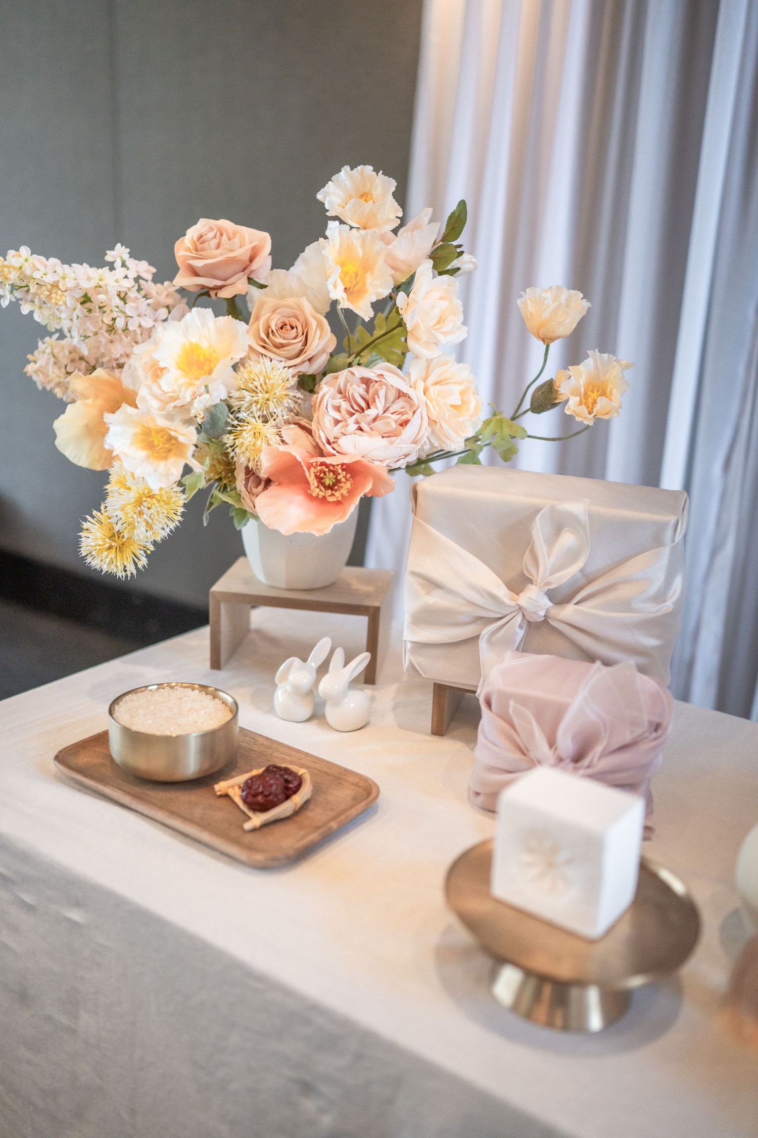 Four images showing a progression of elegant floral arrangements with peach roses and white gift boxes on a marble surface for a Dohl.