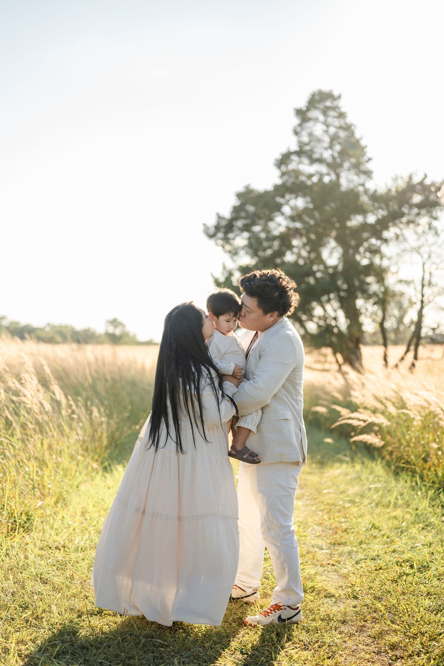 Family enjoying tender moment together in sunny meadow with golden light and tall grass at sunset.