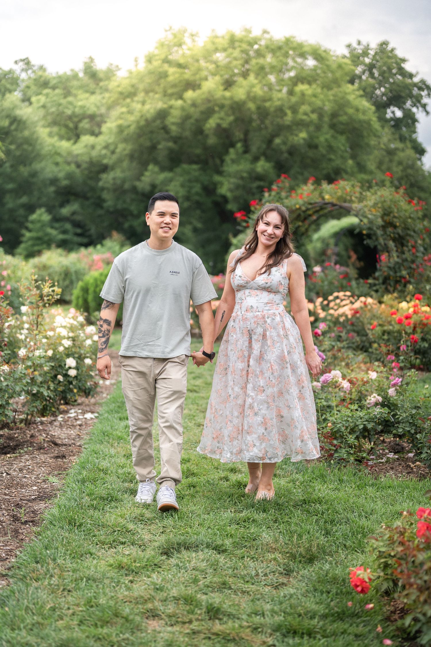 A couple takes a romantic stroll along a garden path surrounded by blooming roses. Sterling Family Photographer
