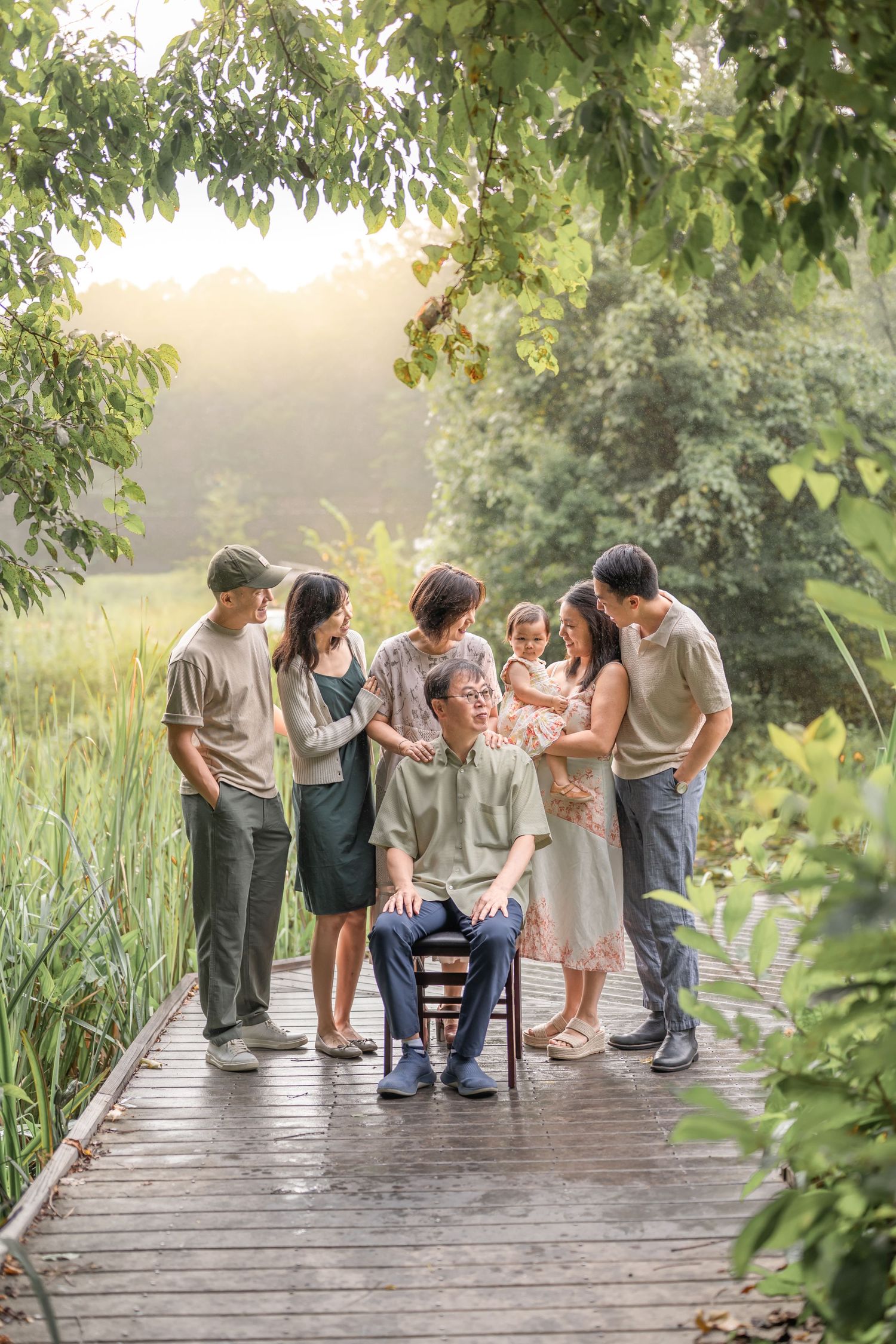 Group gathers on a rustic wooden boardwalk surrounded by lush greenery during a summer photoshoot.