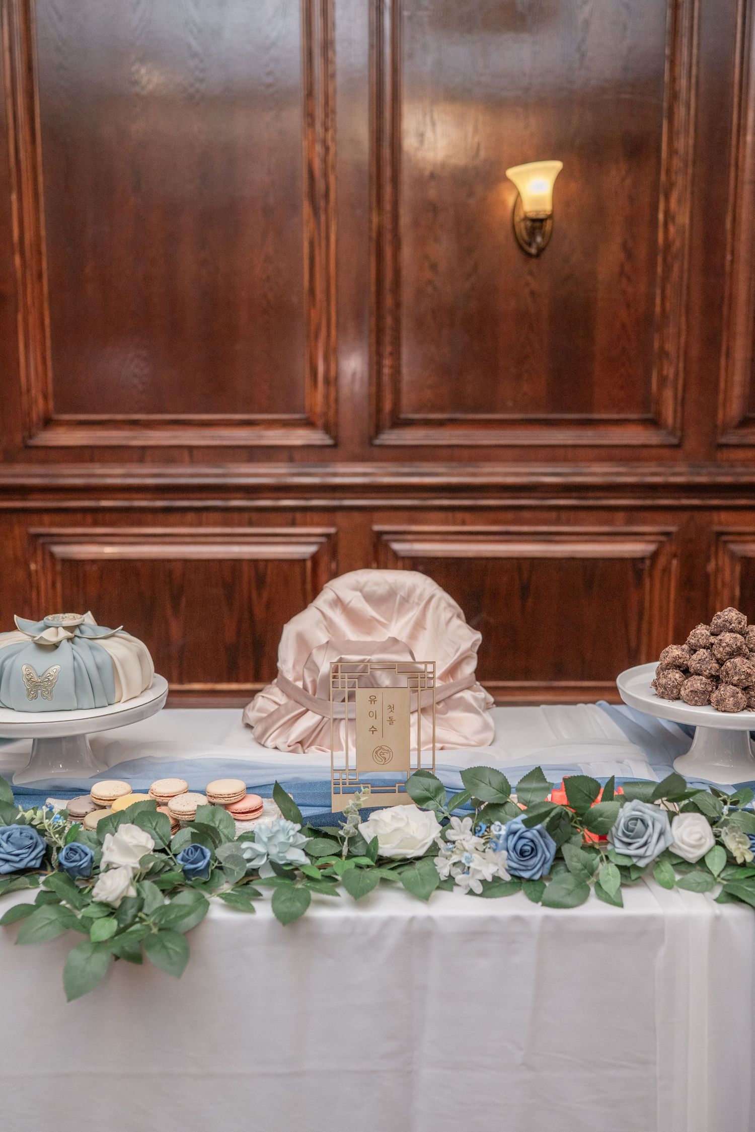 Elegant banquet table setting with white linens and blue floral greenery garland decorating the front edge.