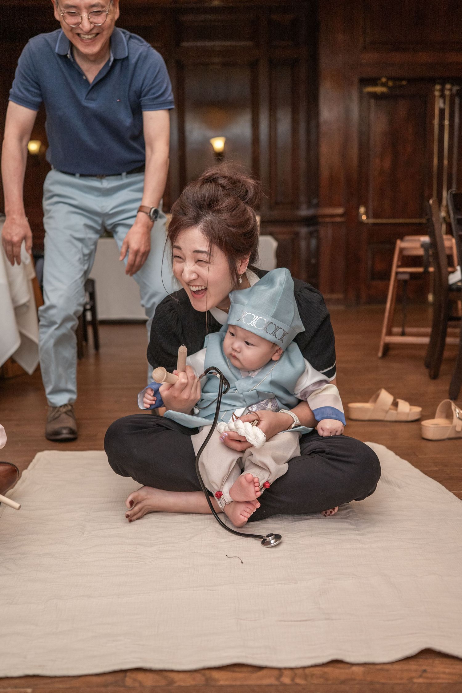 People gathering around a blanket on wooden floor during what appears to be a playful moment.