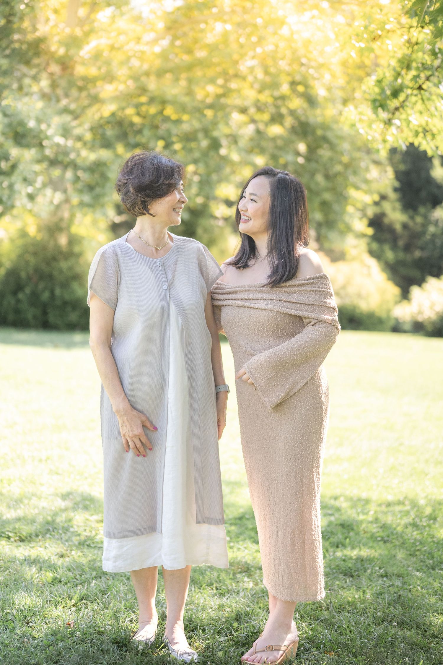 Joyful interaction between two figures wearing neutral tones in a sunny outdoor setting with natural greenery.