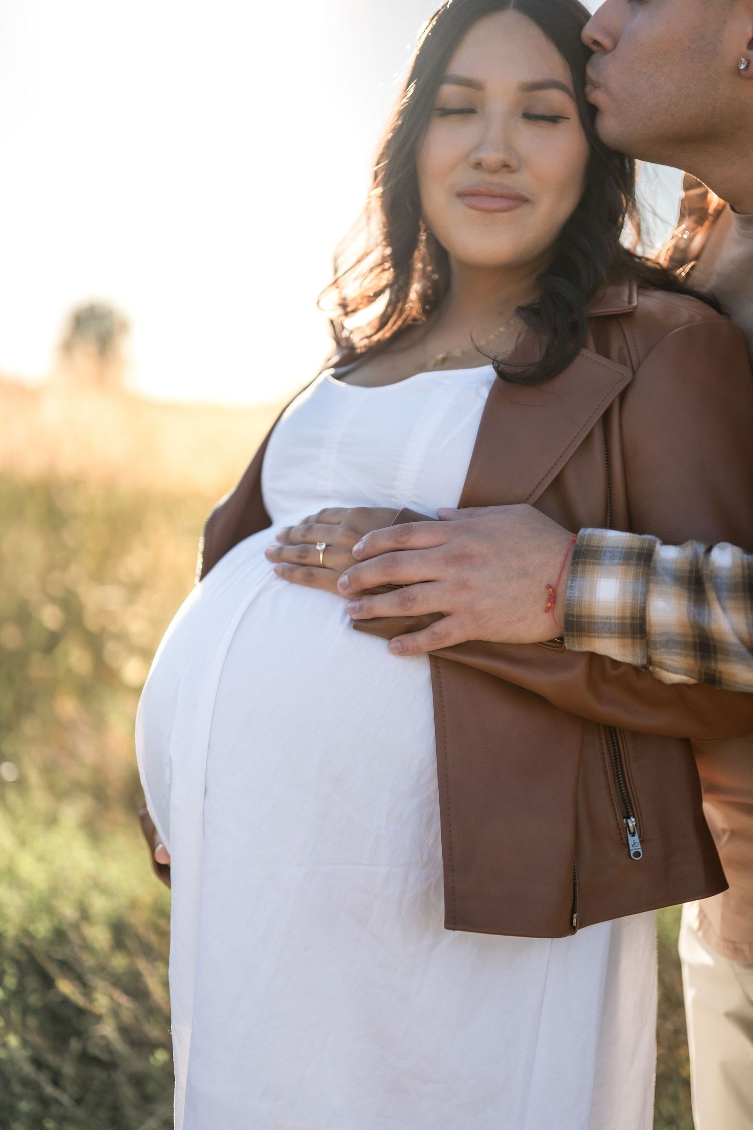 Romantic couple in white and brown outfits embrace tenderly during outdoor golden hour photo session.