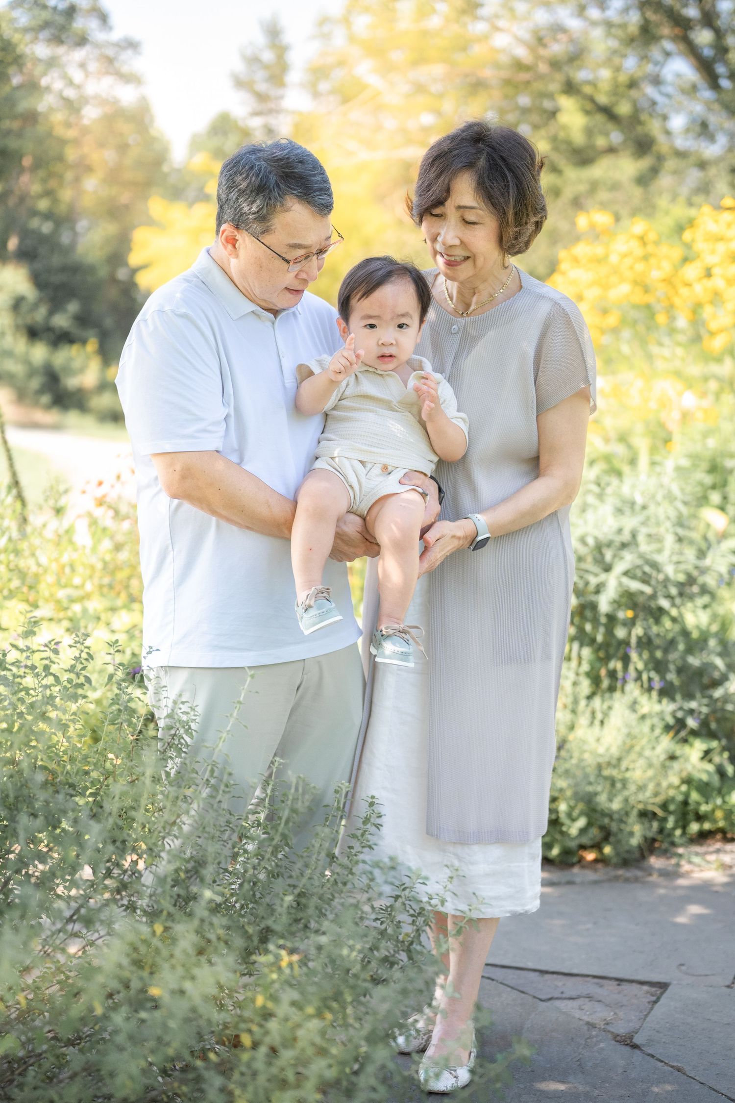 Three heartwarming photographs show a tender outdoor family moment on a sunlit path with greenery and golden foliage.