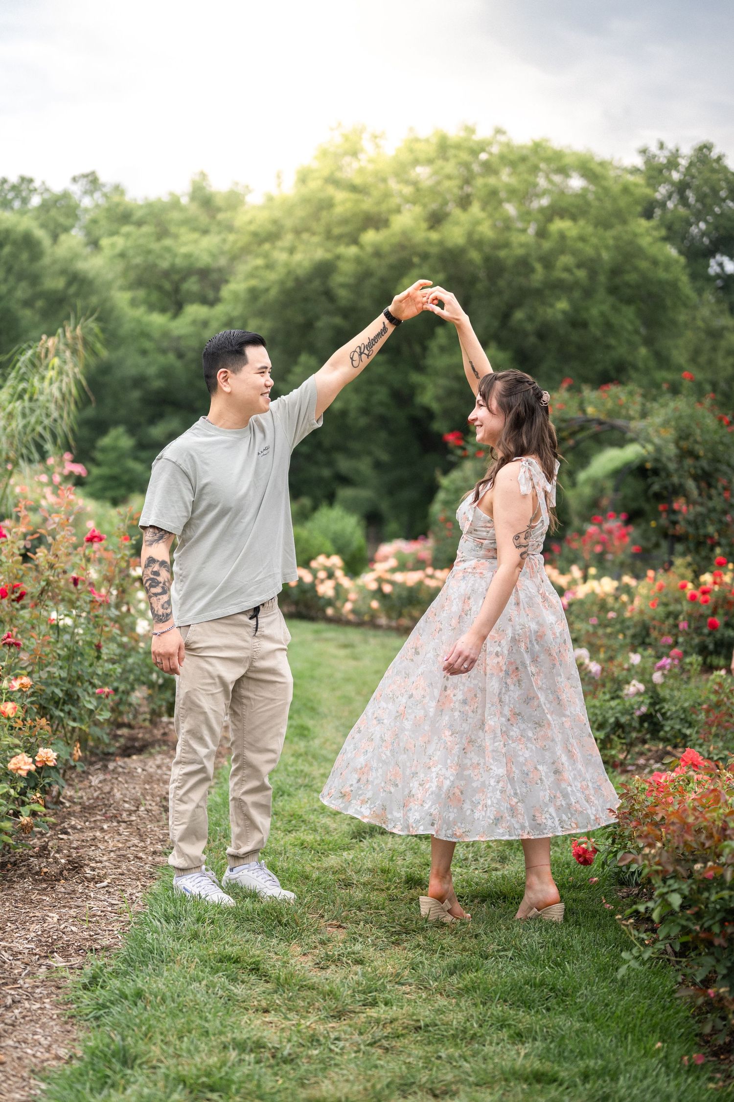 Two people dance together joyfully in a blooming garden filled with colorful roses and lush greenery. engagement Taylor Swift Travis Kelce