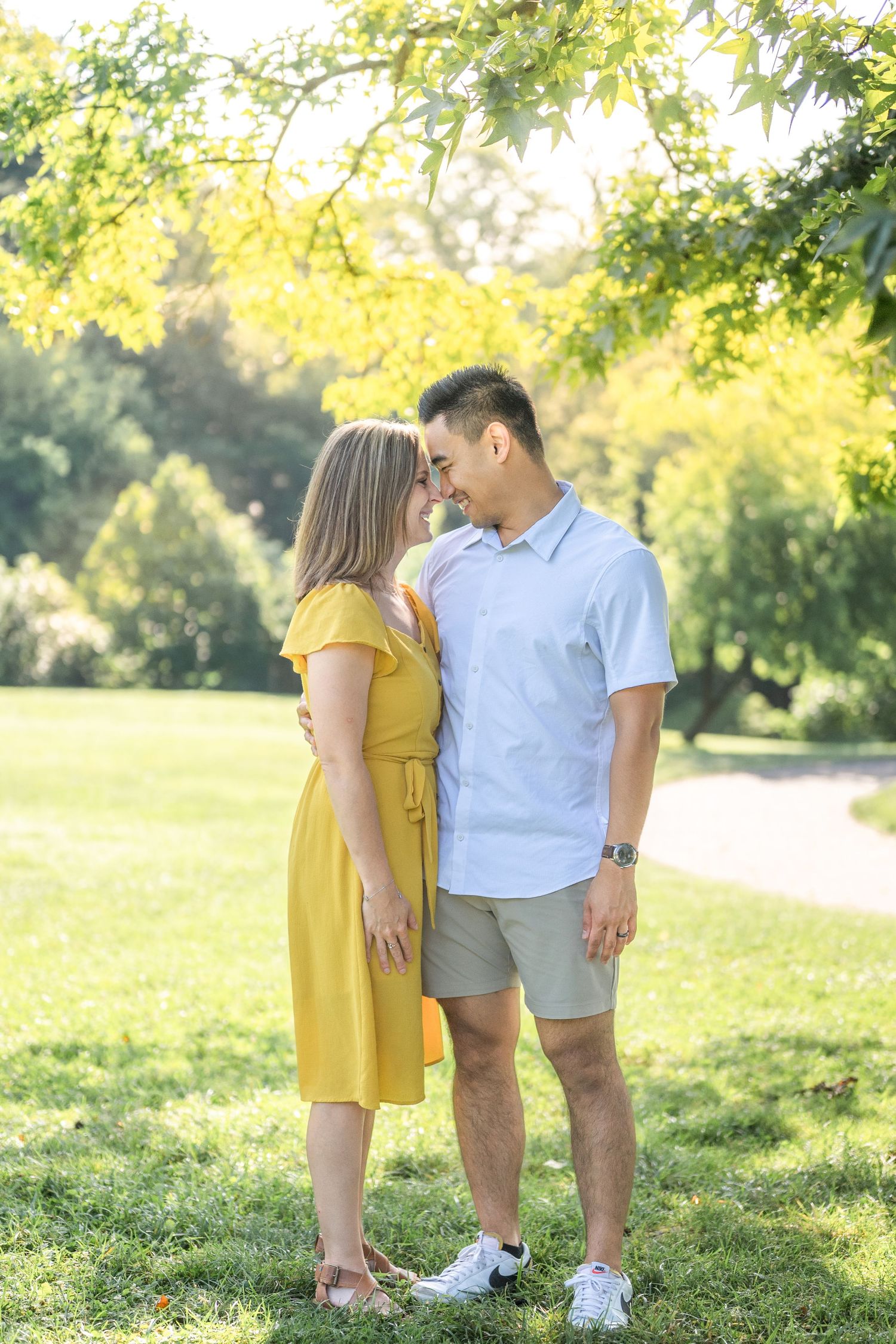 A couple in a yellow dress and white shirt share tender moments in a sun-dappled park setting. Alexandria photographer