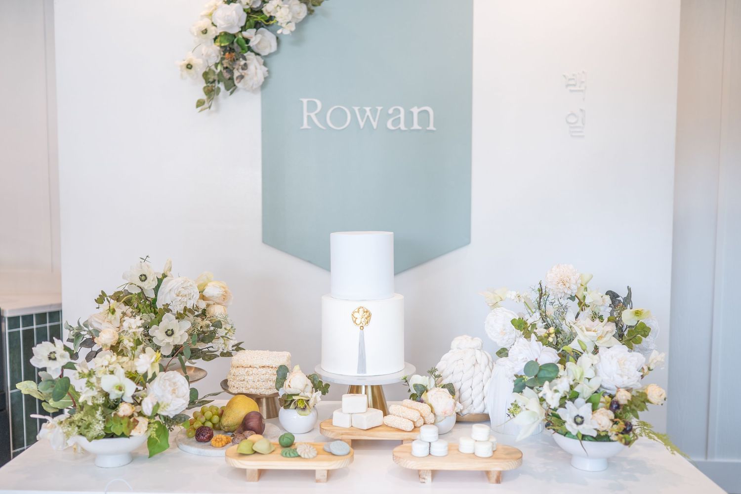 Elegant white and sage green party decor with floral arrangements and balloons in a modern indoor setting.