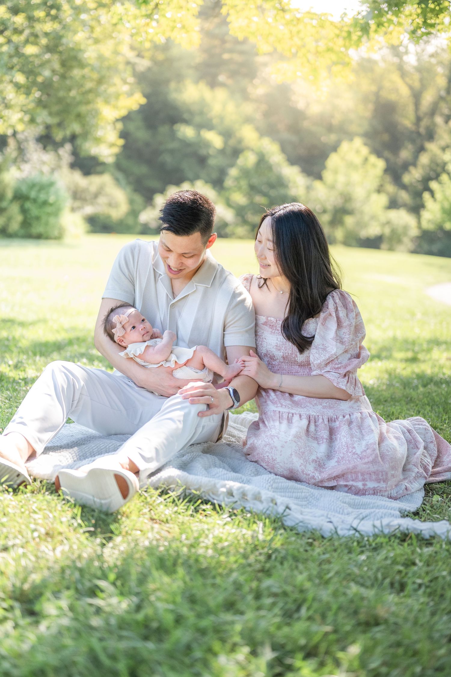 Family enjoying a tender moment together on a blanket in a sunny park during a warm summer afternoon. Photographer