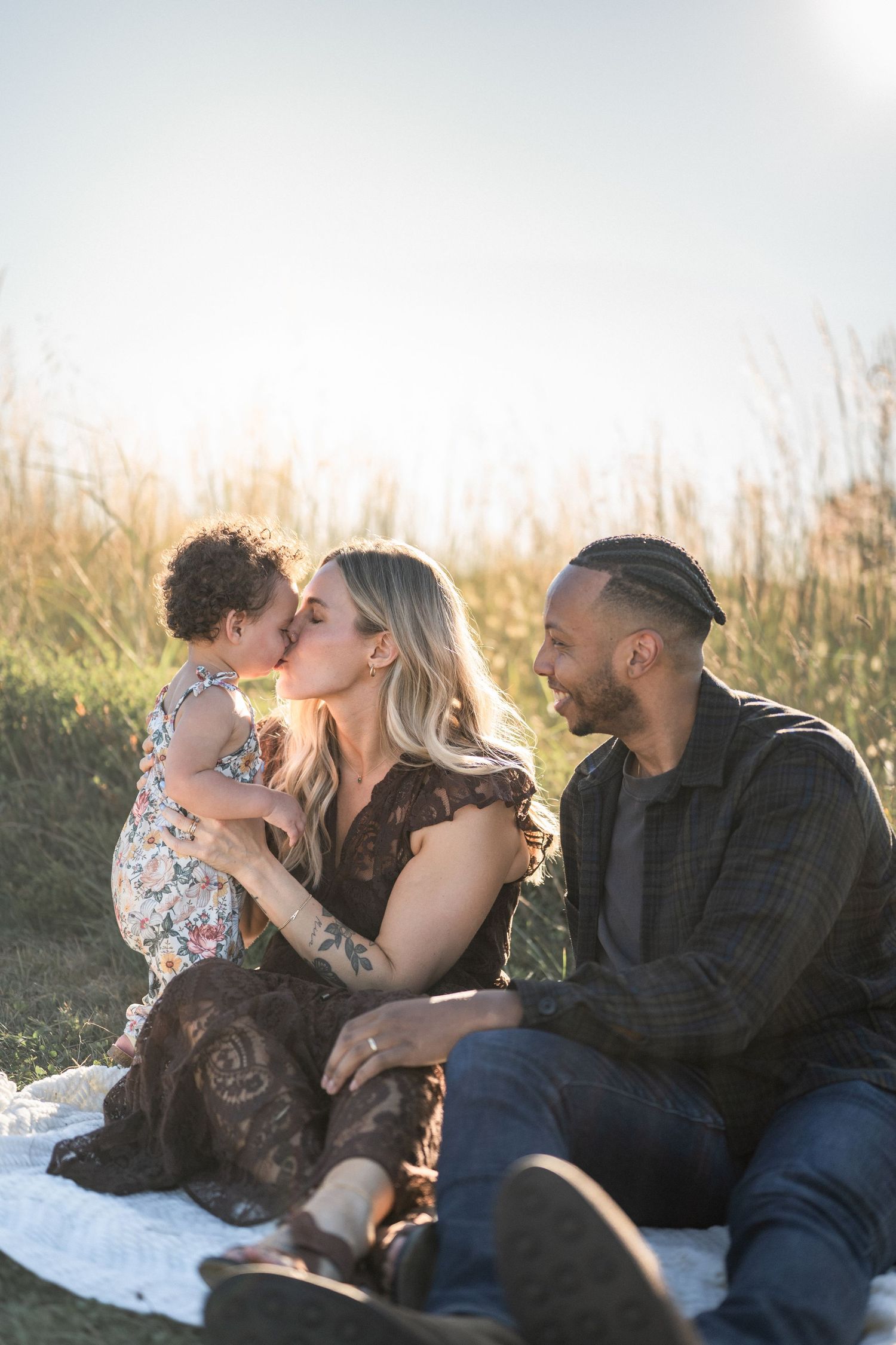 A family relaxes together on a blanket in a golden field during sunset.