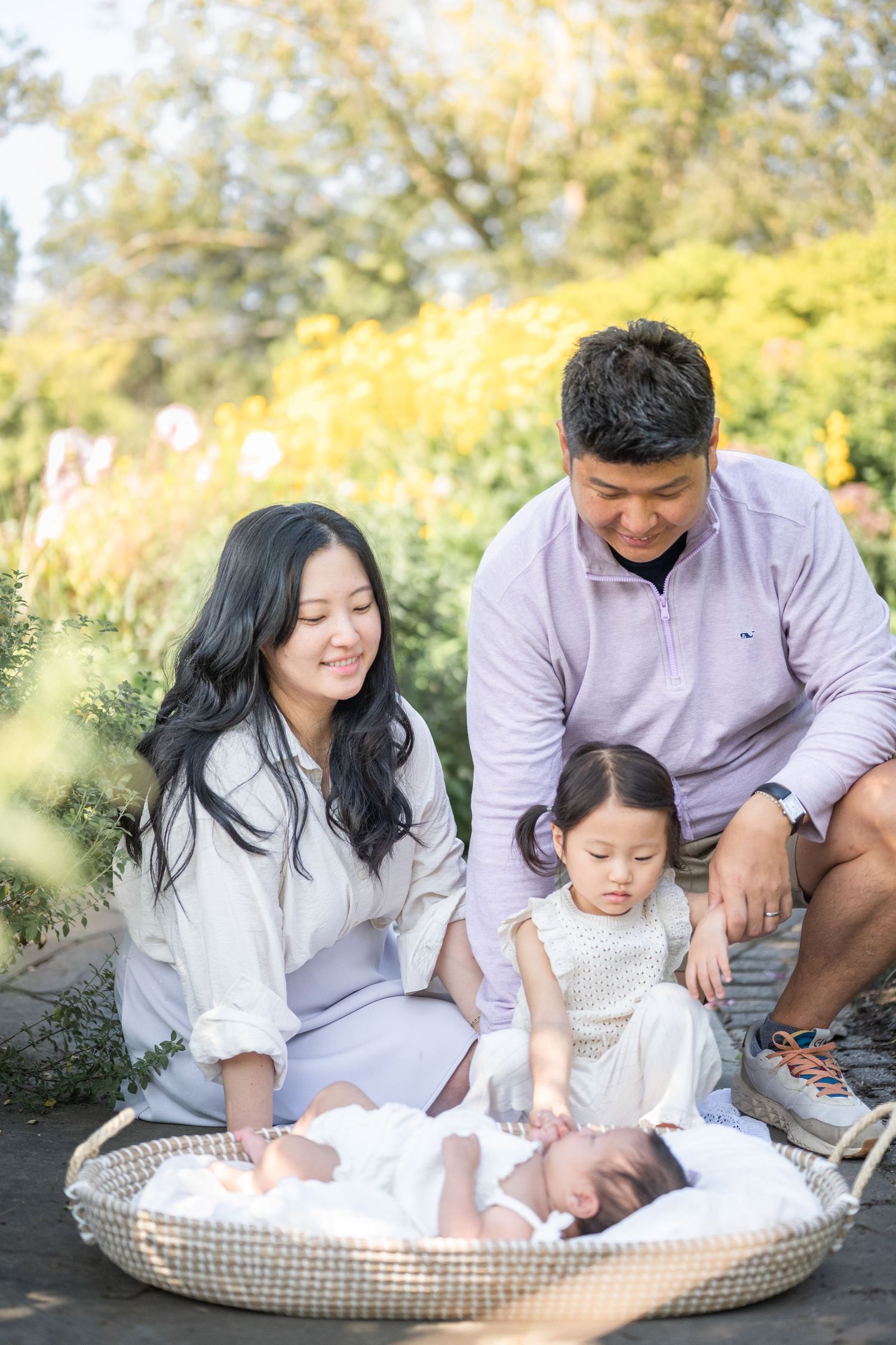 Family shares tender moment outdoors on sunny day with baby resting in basket surrounded by autumn foliage. Virginia photographer