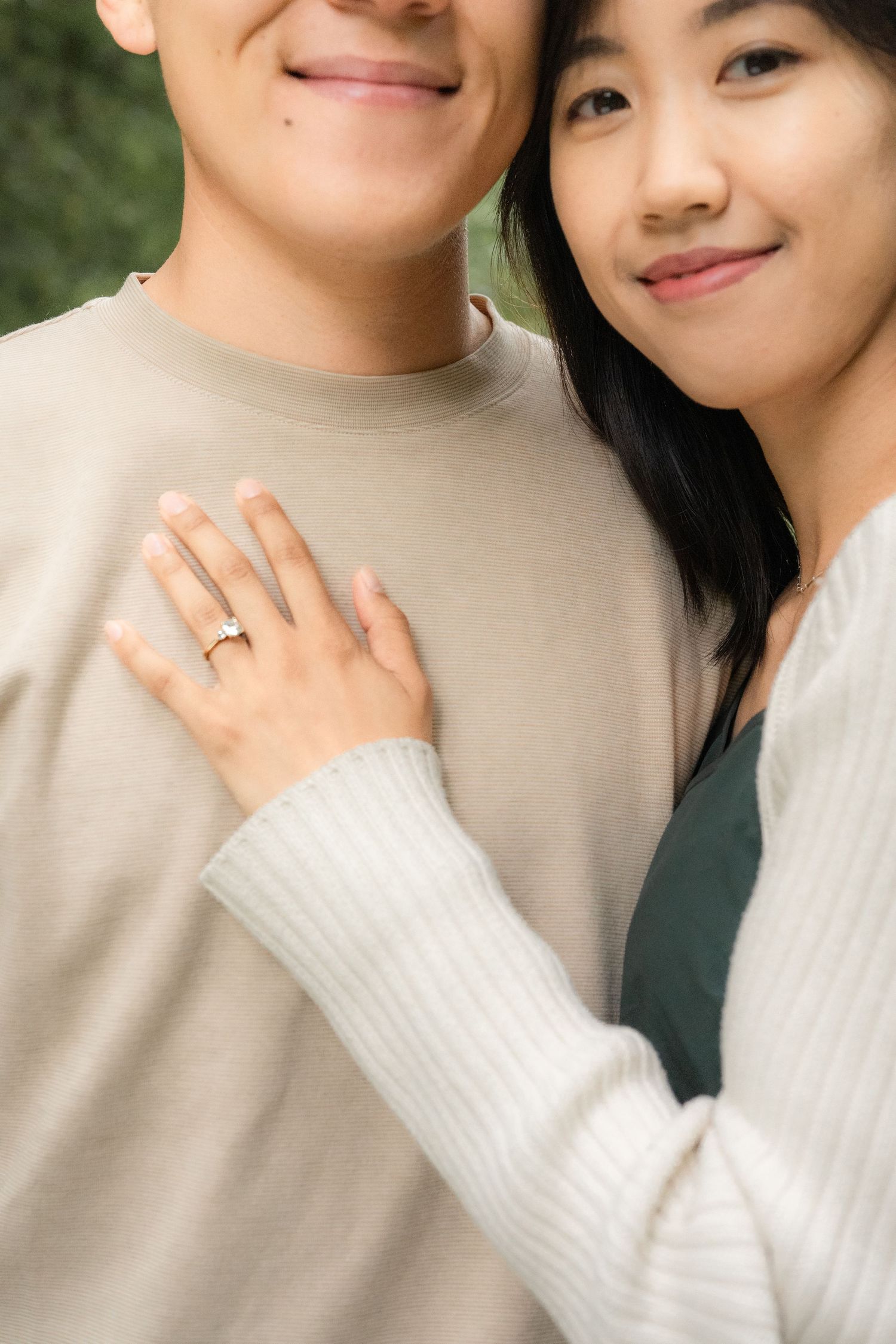 A close-up shot showing a person's hand with an engagement ring resting on someone wearing a beige sweater.