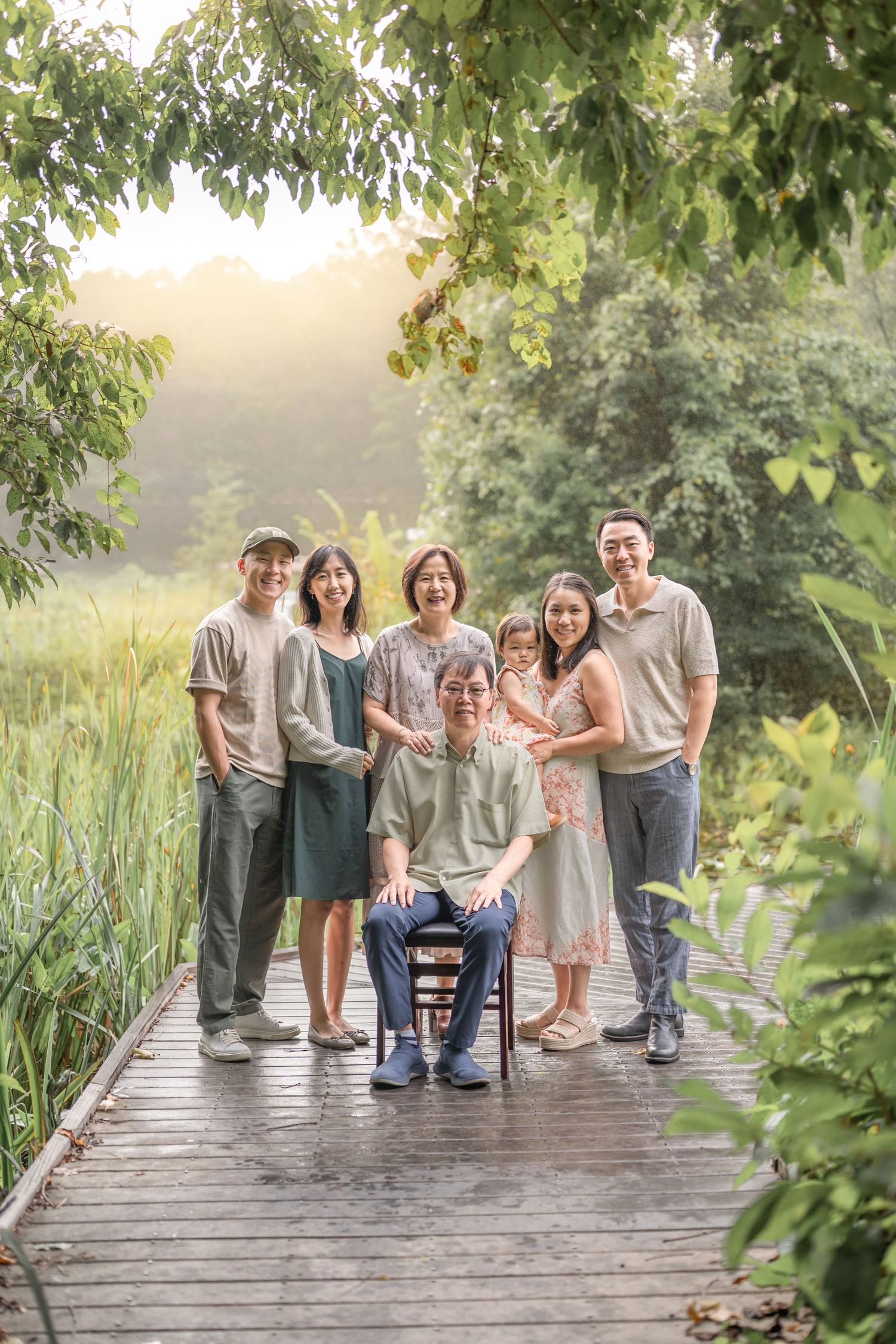 A group sits together on a wooden boardwalk surrounded by lush greenery during a summer photo session.