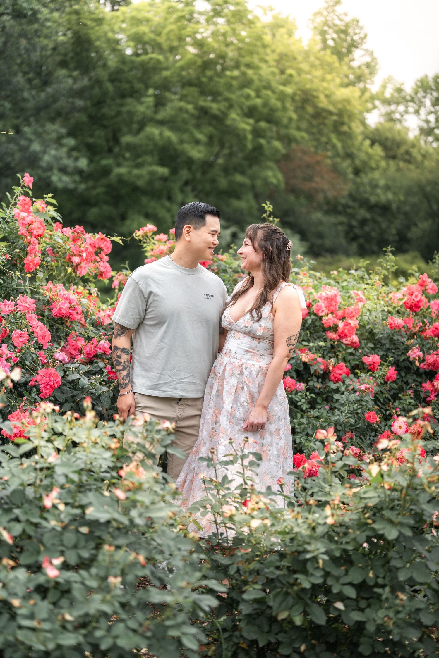 A romantic moment captured between a couple standing among blooming pink rose bushes in a garden. Alexandria Family Photographer Taylor Swif