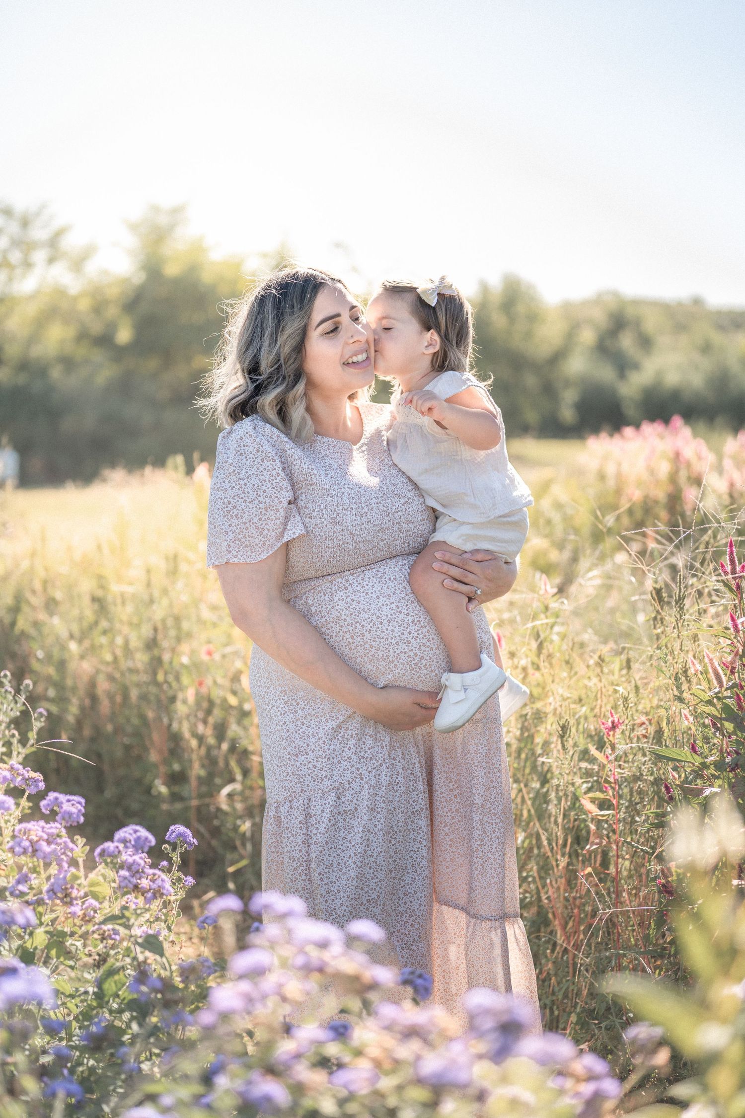 A loving embrace is shared between parent and child in a sunlit meadow filled with purple wildflowers.