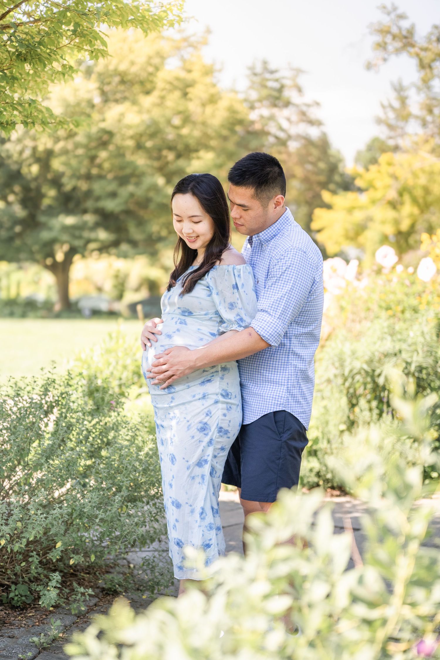 A couple embraces lovingly in a sun-drenched garden with wildflowers and greenery creating a romantic backdrop. Arlington photographer