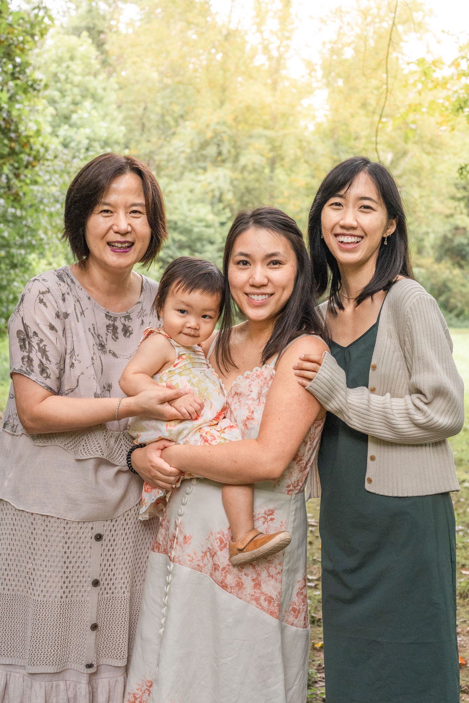 A group gathers outdoors for photos with a warm natural backdrop of trees and filtered sunlight.