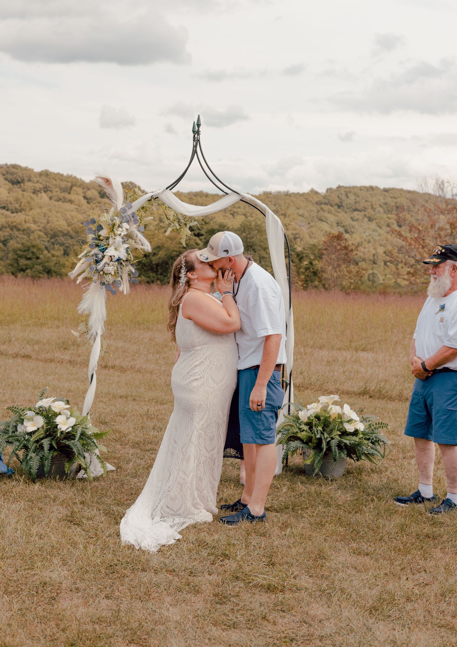 Bride and groom sharing their first kiss under a rustic boho arch at an outdoor fall wedding.