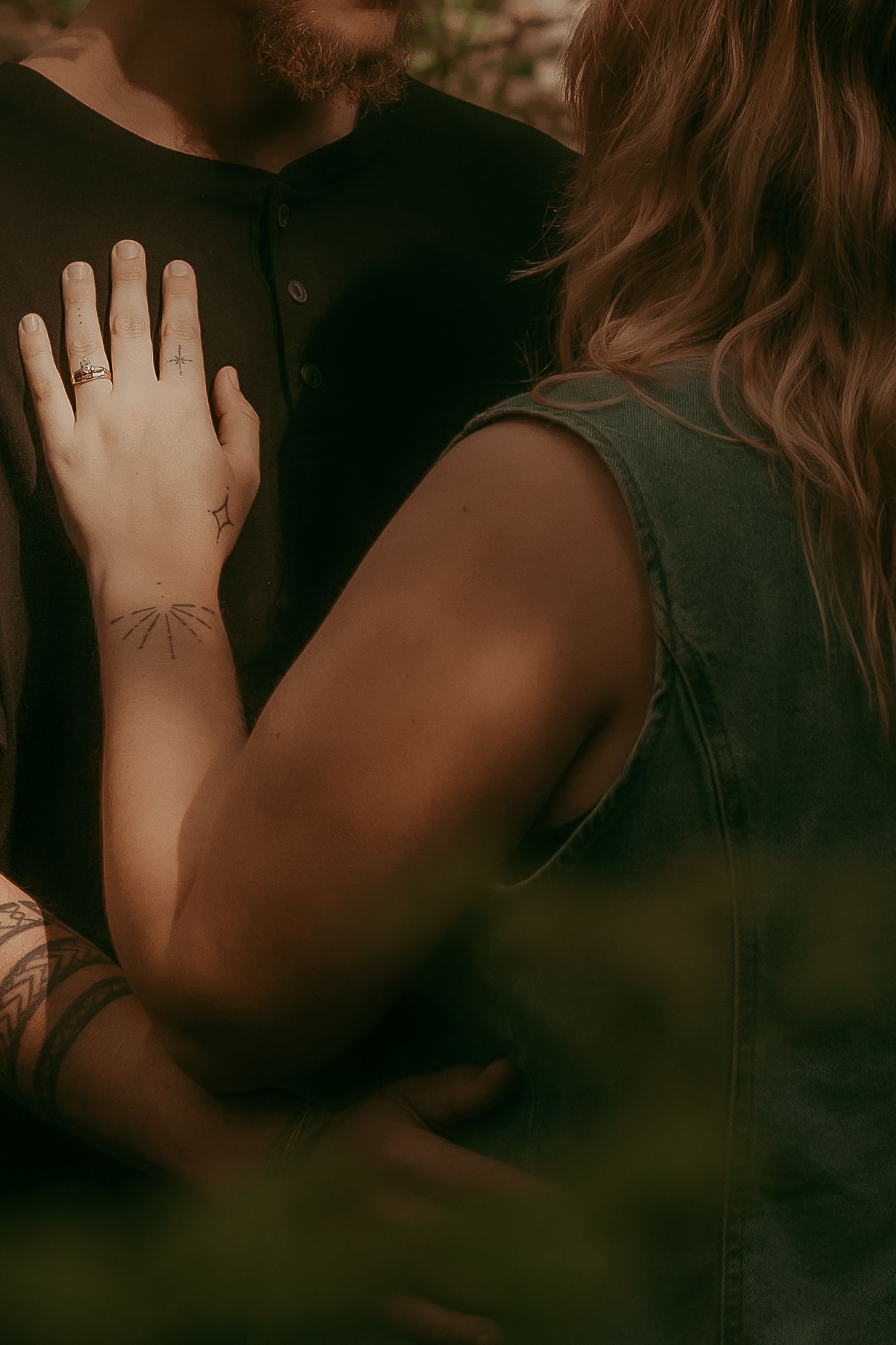 Close-up of woman placing tattooed hand on partners chest showing engagement ring.