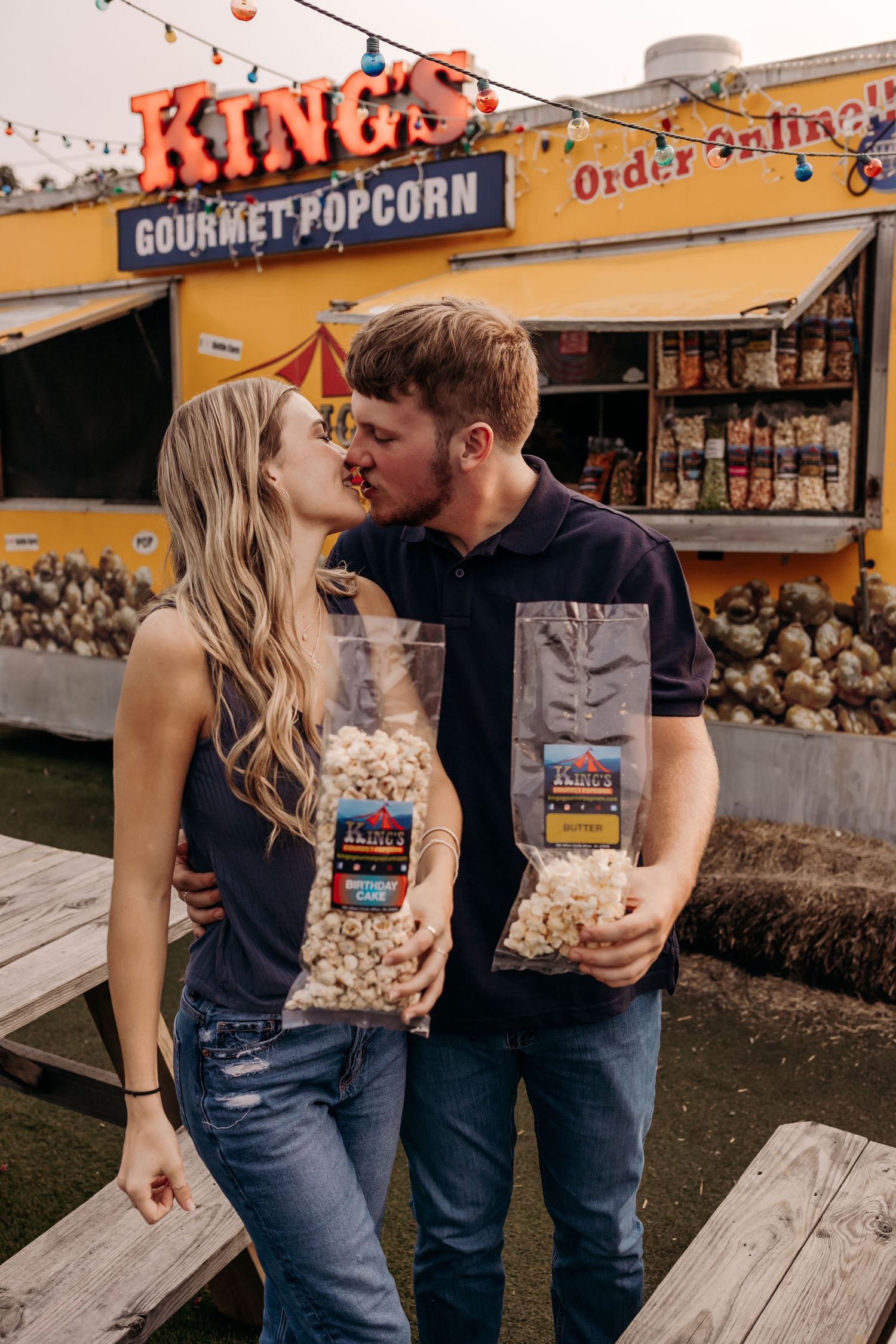 Couple kissing while holding bags of King's Gourmet Popcorn outside the colorful popcorn stand.